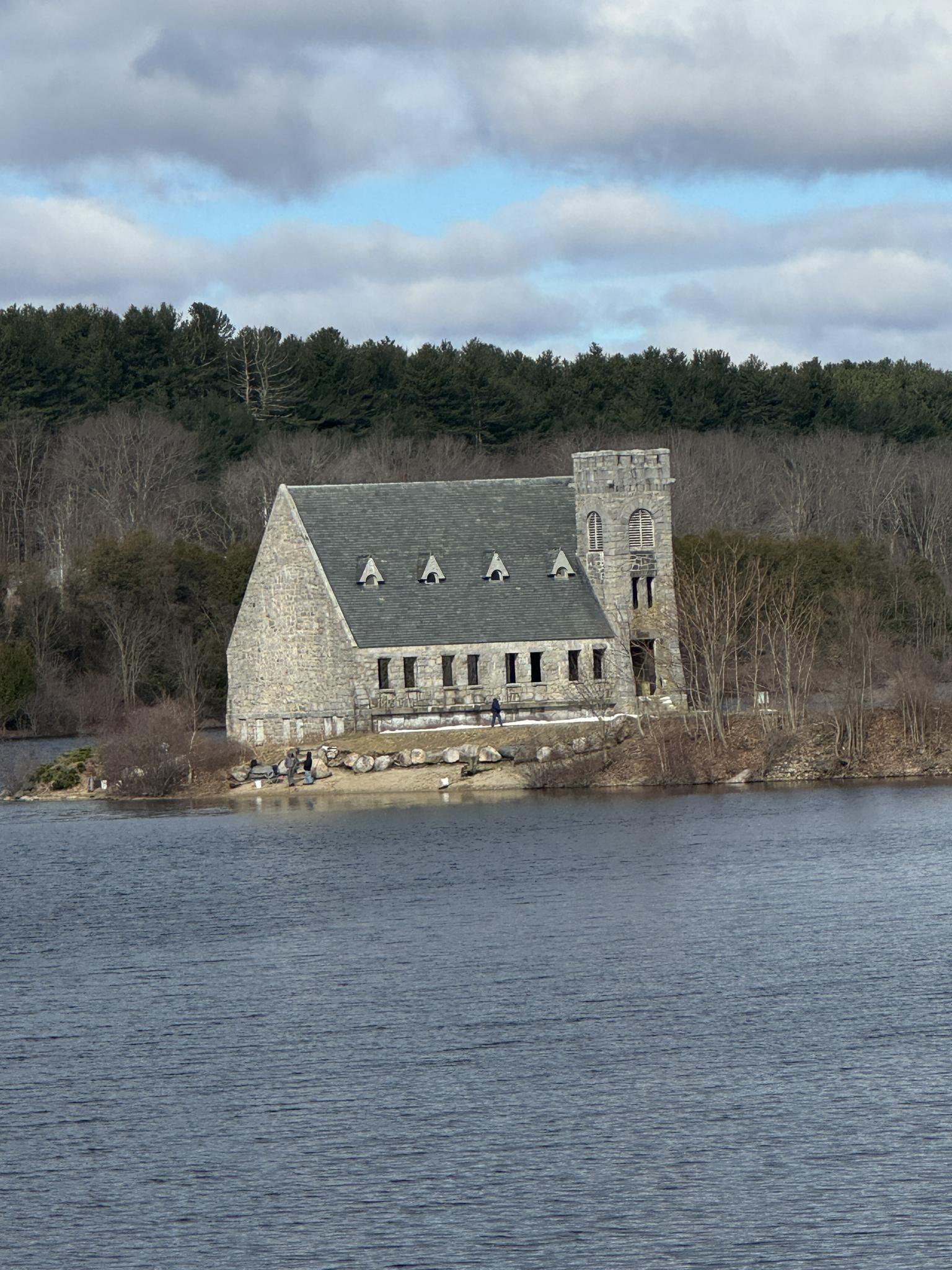 Stone building with a tower on a lake island under a cloudy sky.