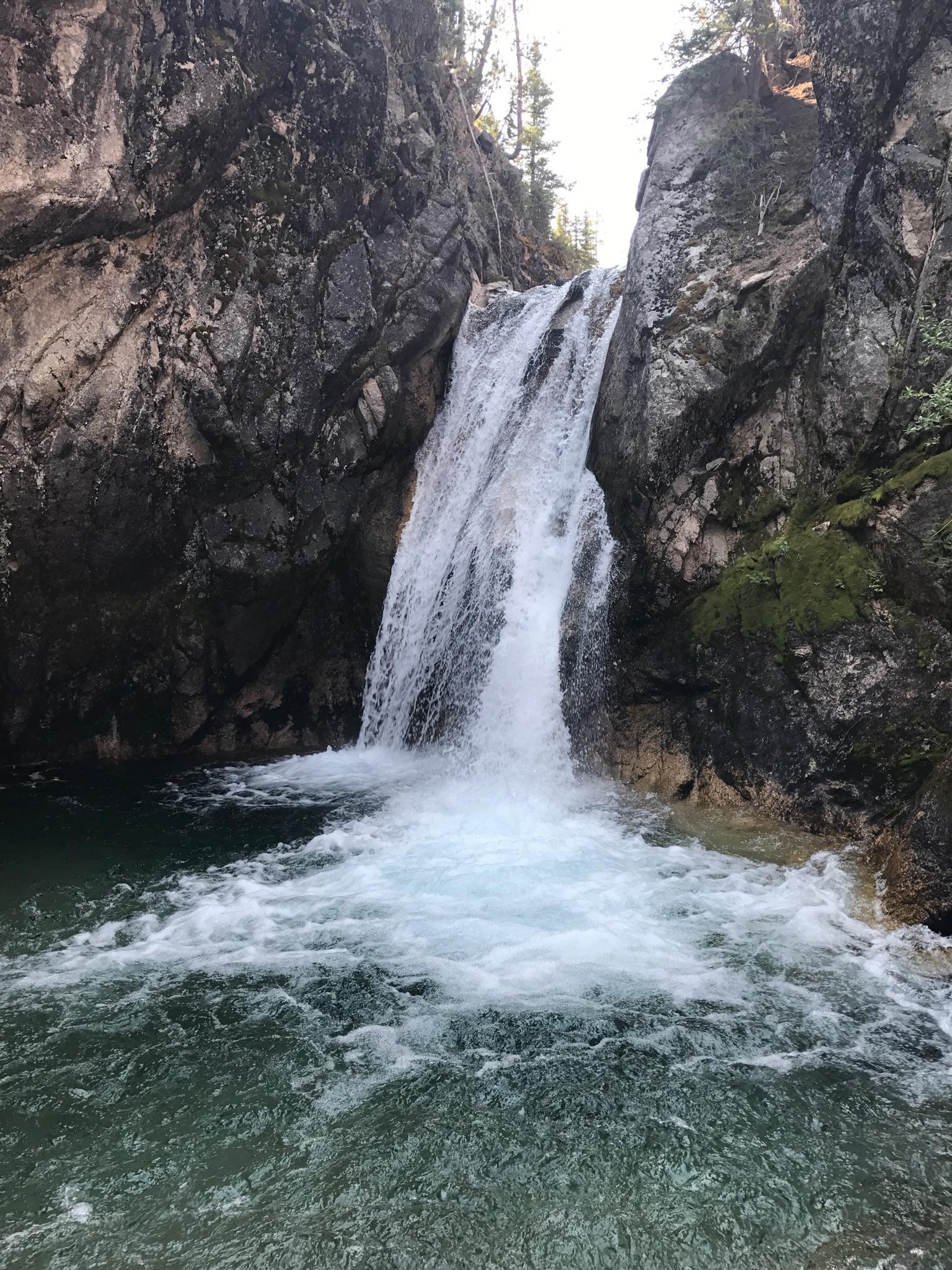 A powerful waterfall cascades over dark rocks into a clear, bubbling pool below.