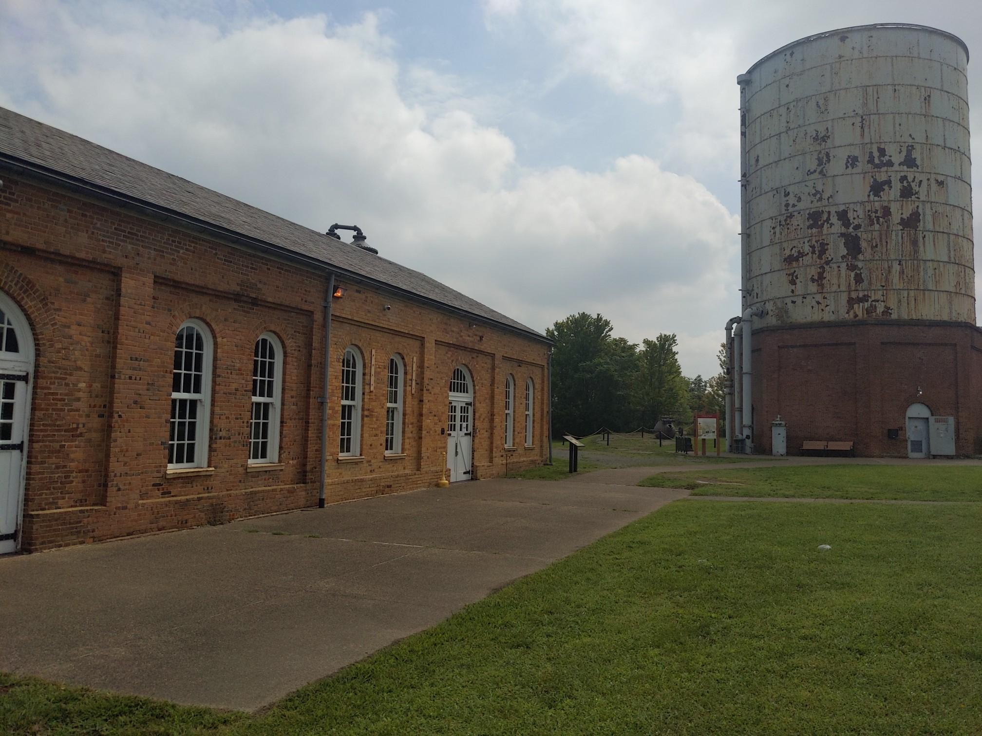 A brick building and large water tower stand next to a grassy area.