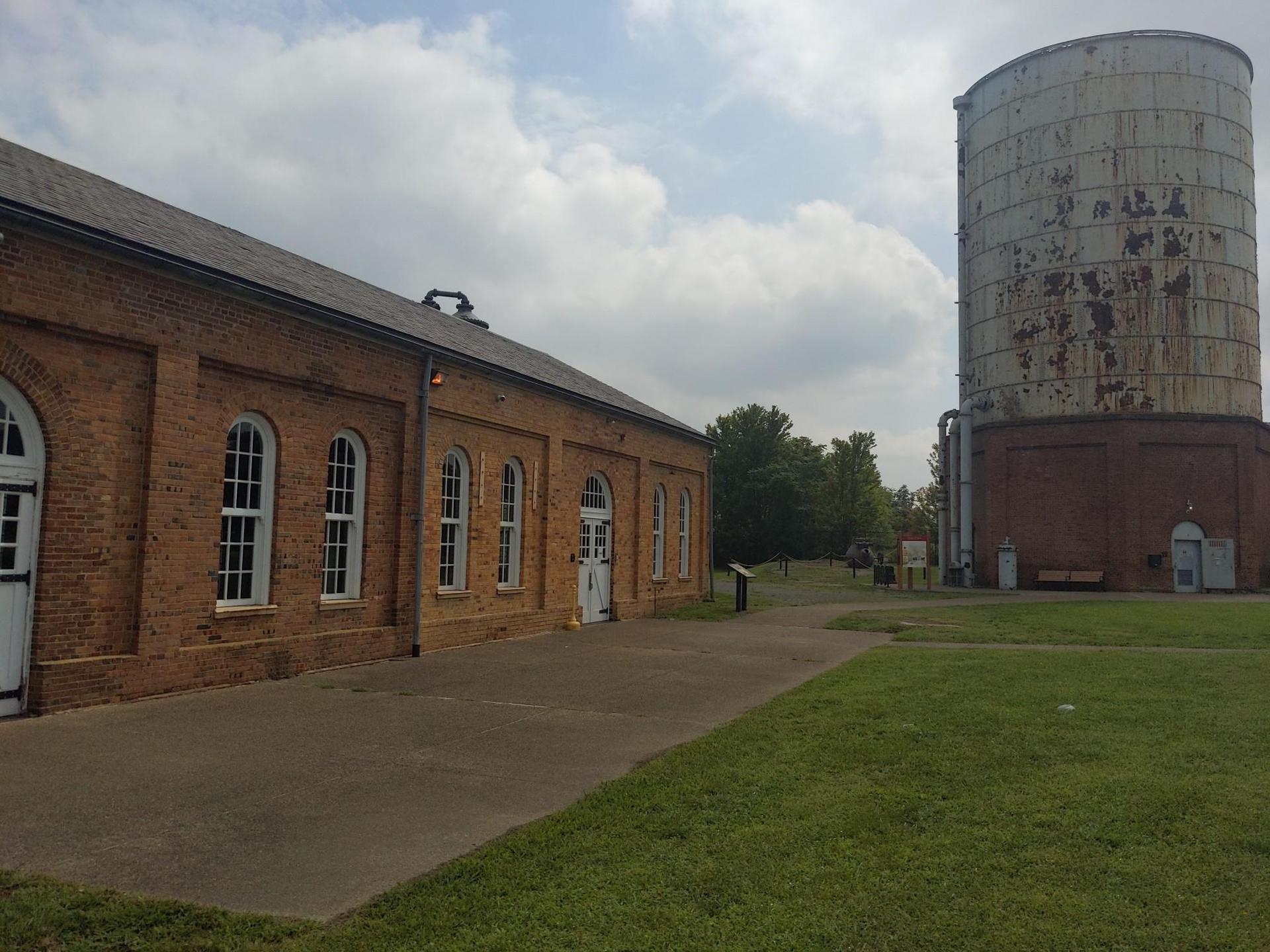 A brick building and large water tower stand next to a grassy area.