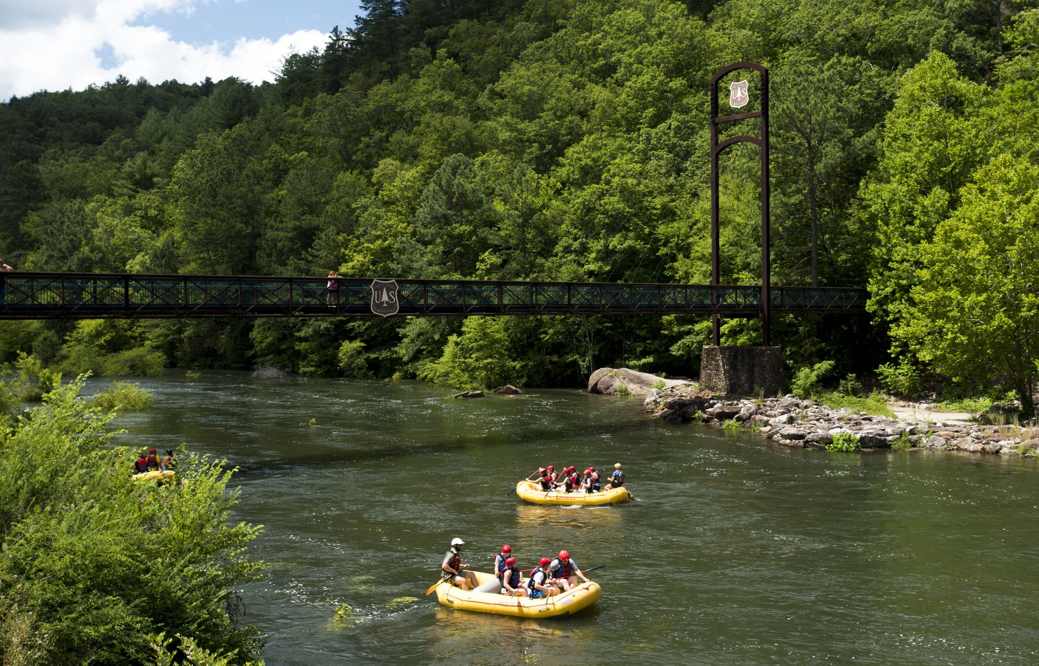 People in yellow rafts paddle down a green river under a bridge. - Whitewater River loop from Ocoee Number Three Lake