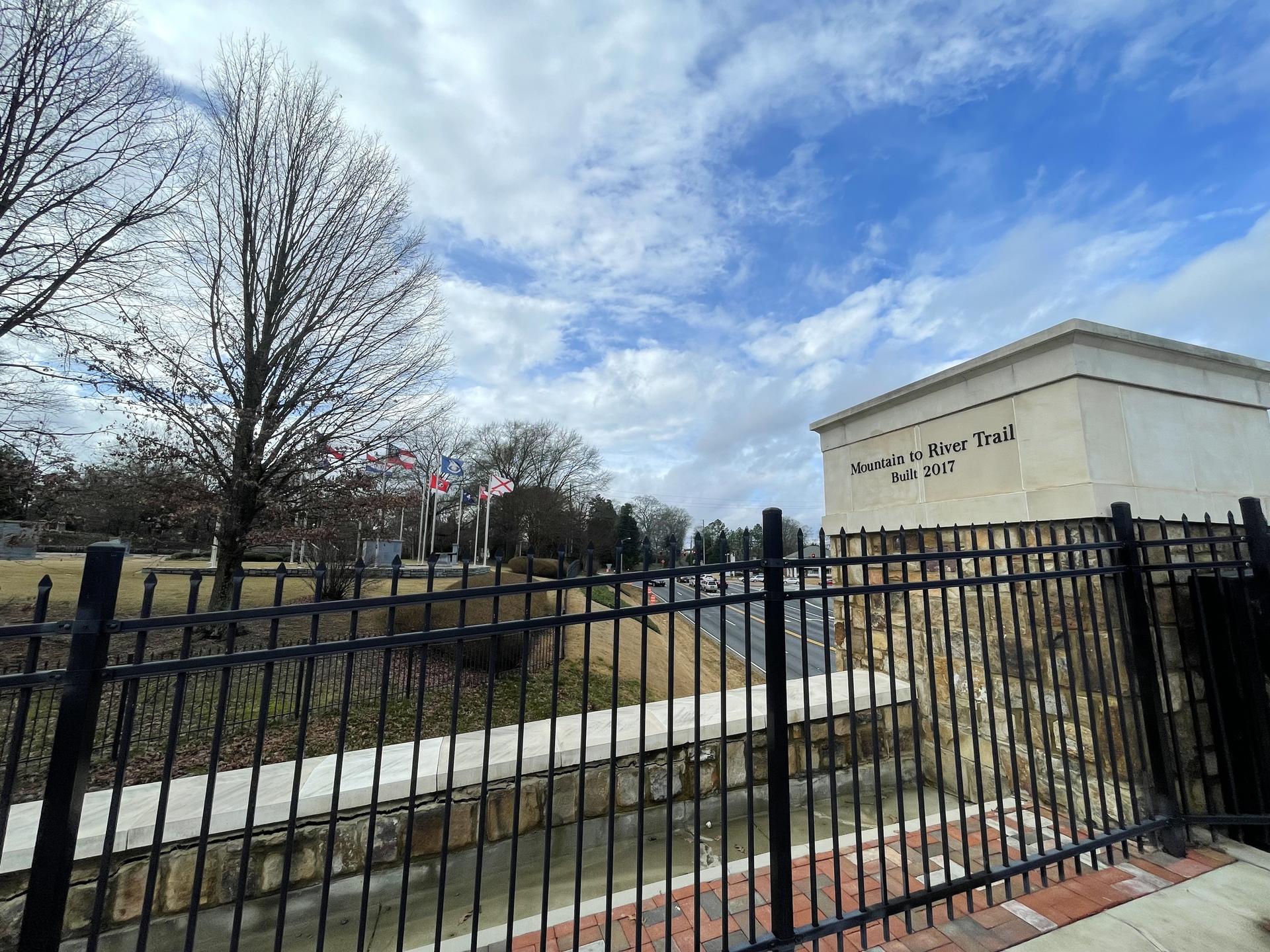 Black fence in foreground, bare trees, building, and flags under cloudy sky.