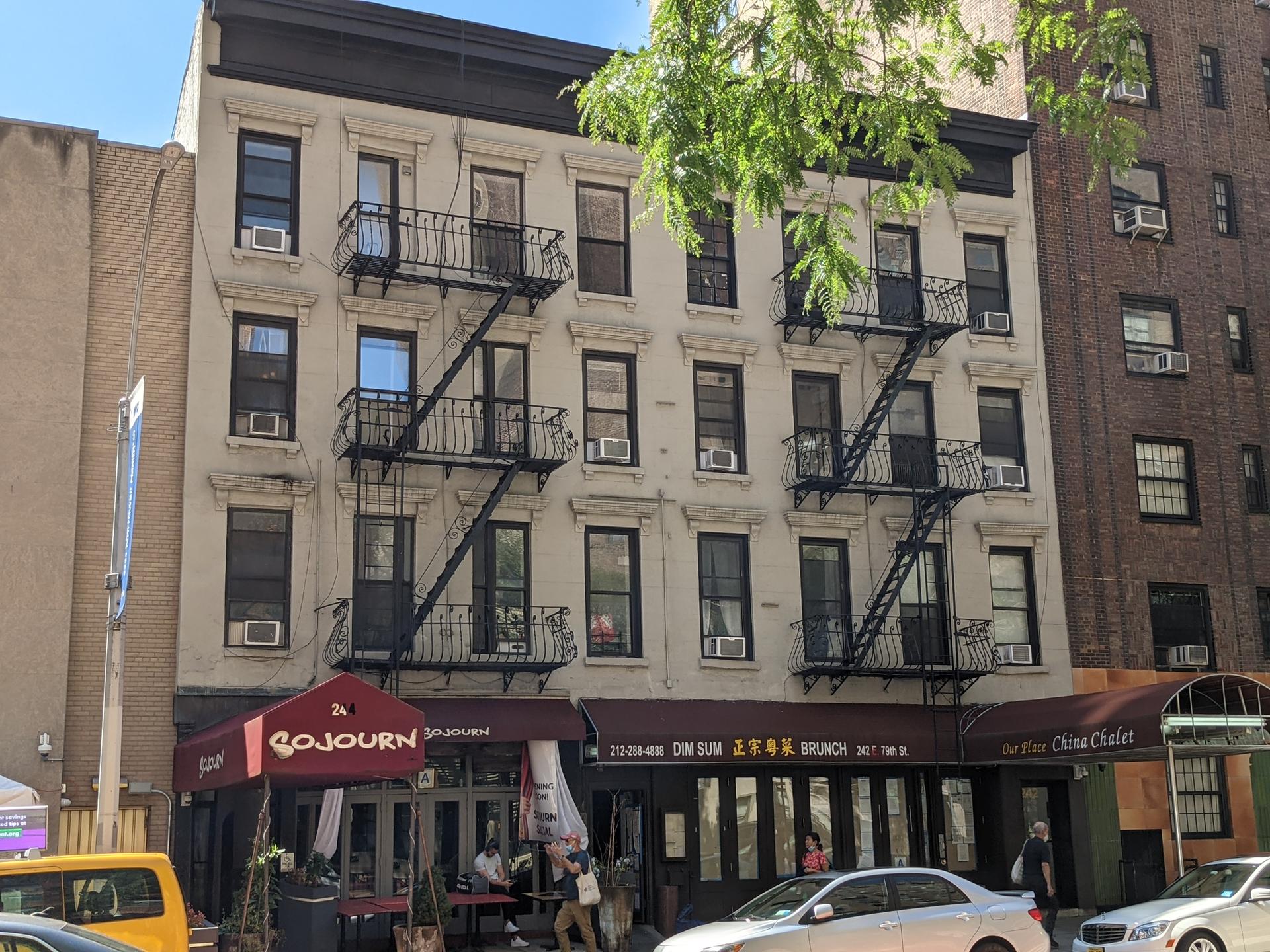 Urban building with fire escapes, storefronts, and people on the sidewalk.