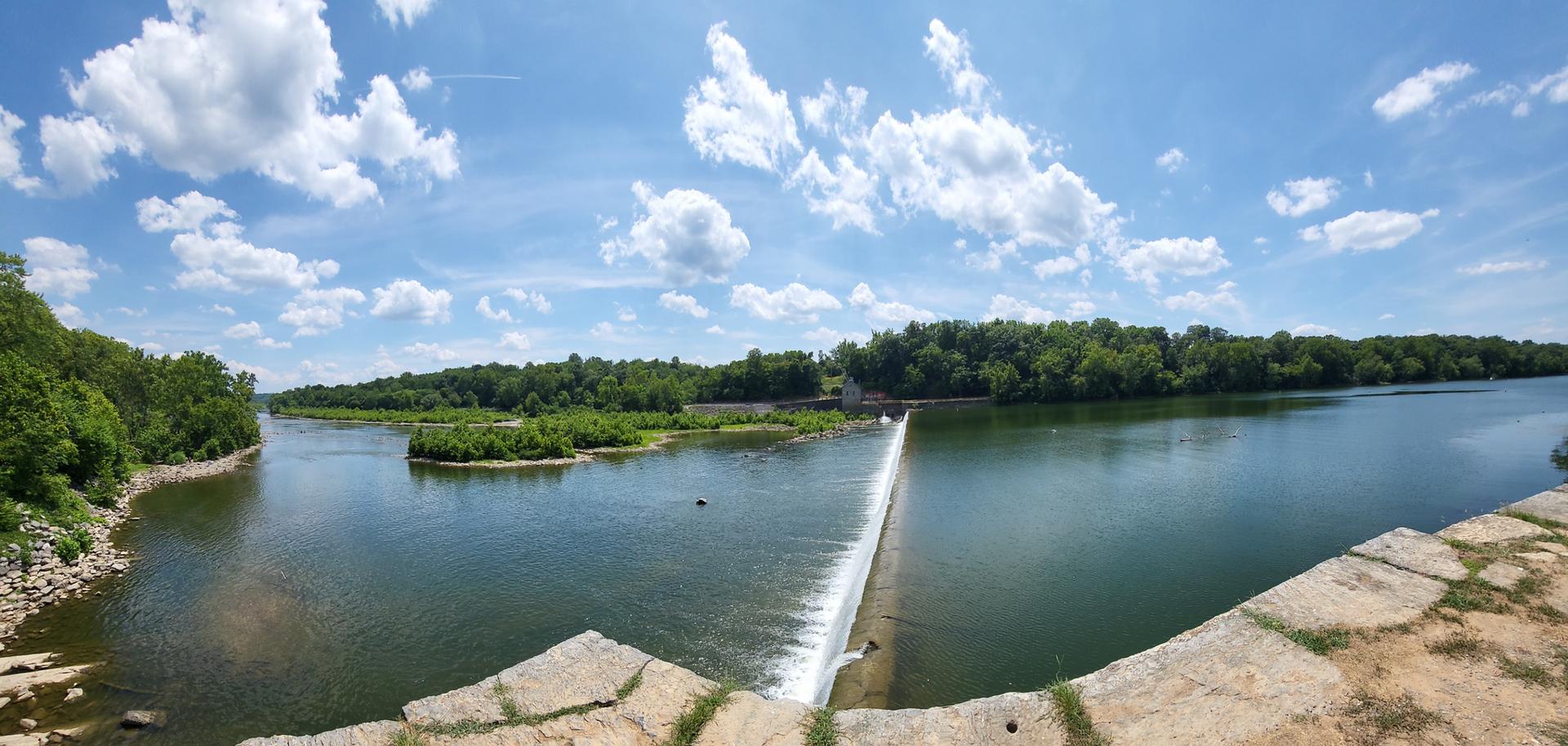 Panoramic view of a wide river with a dam and small islands.