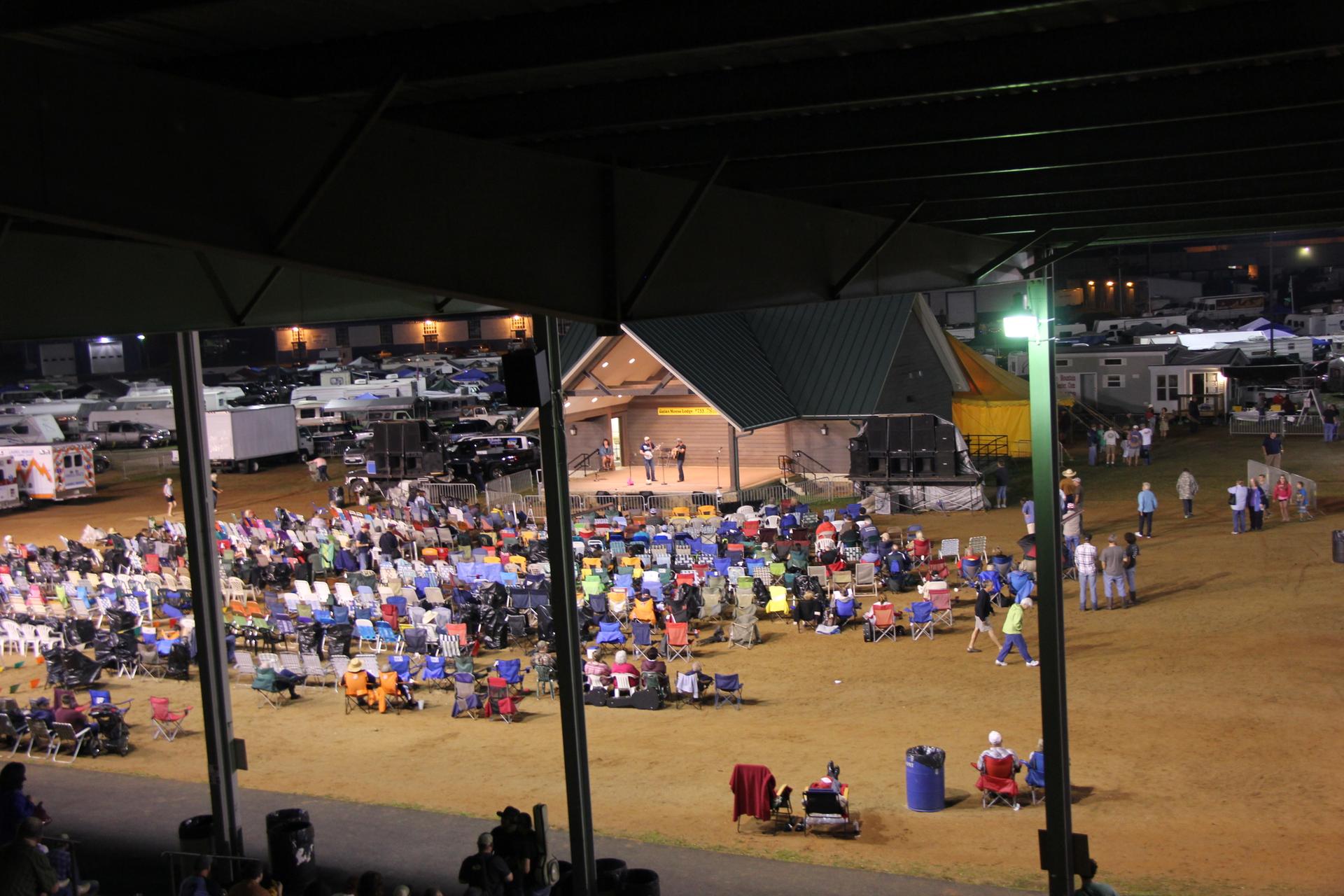 Nighttime view of an outdoor event with many people seated in chairs.