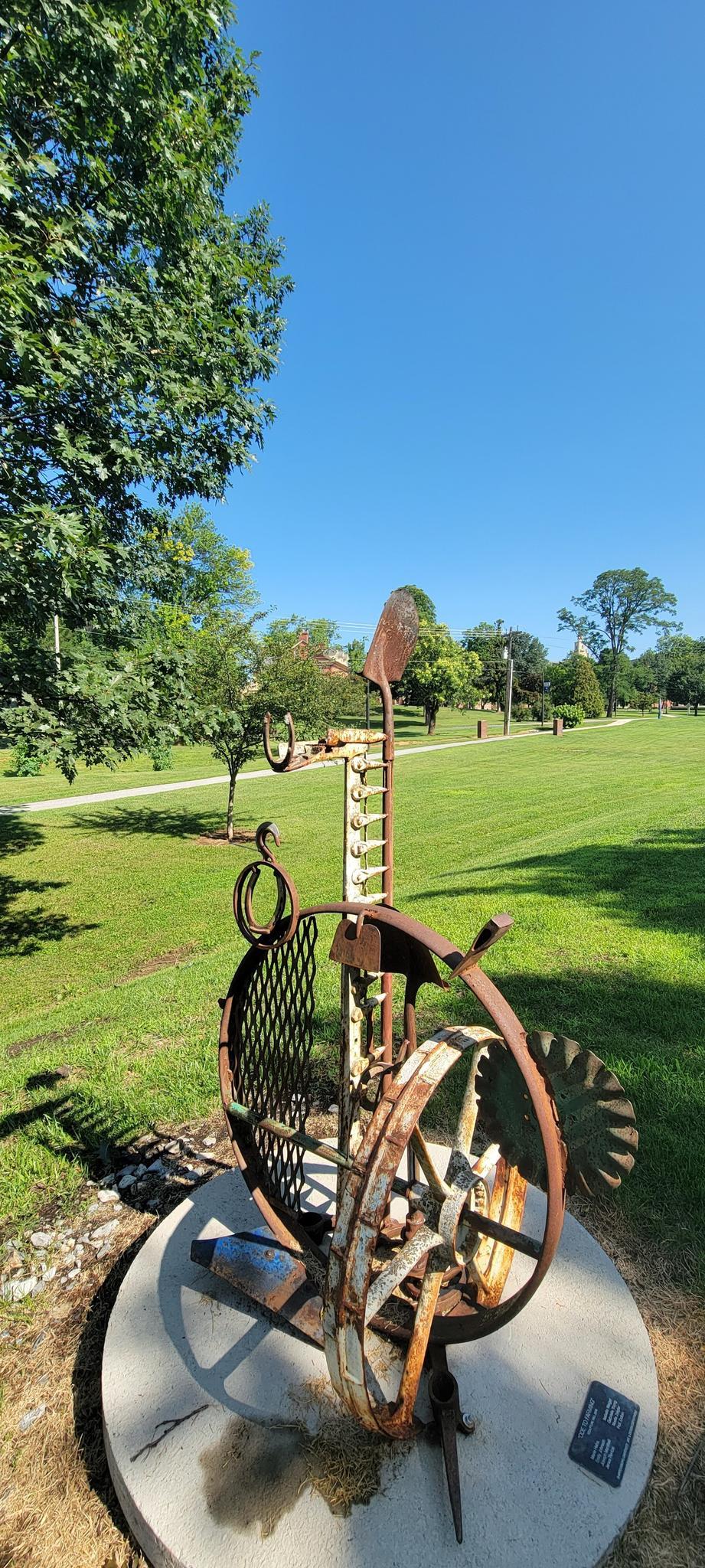 Rustic metal sculpture in a sunny green park under a clear blue sky.