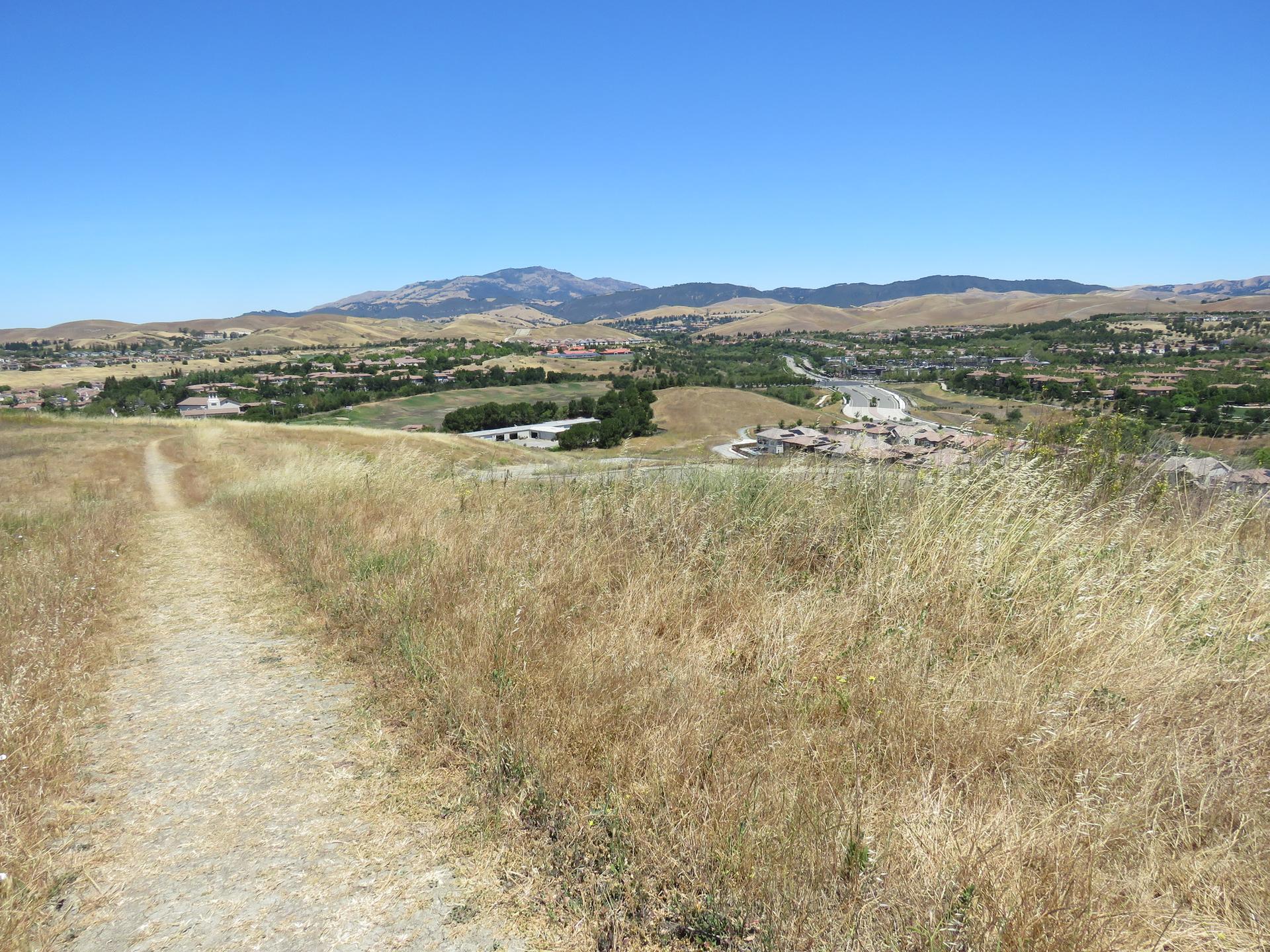 A dirt path through dry golden grass under a clear blue sky.
