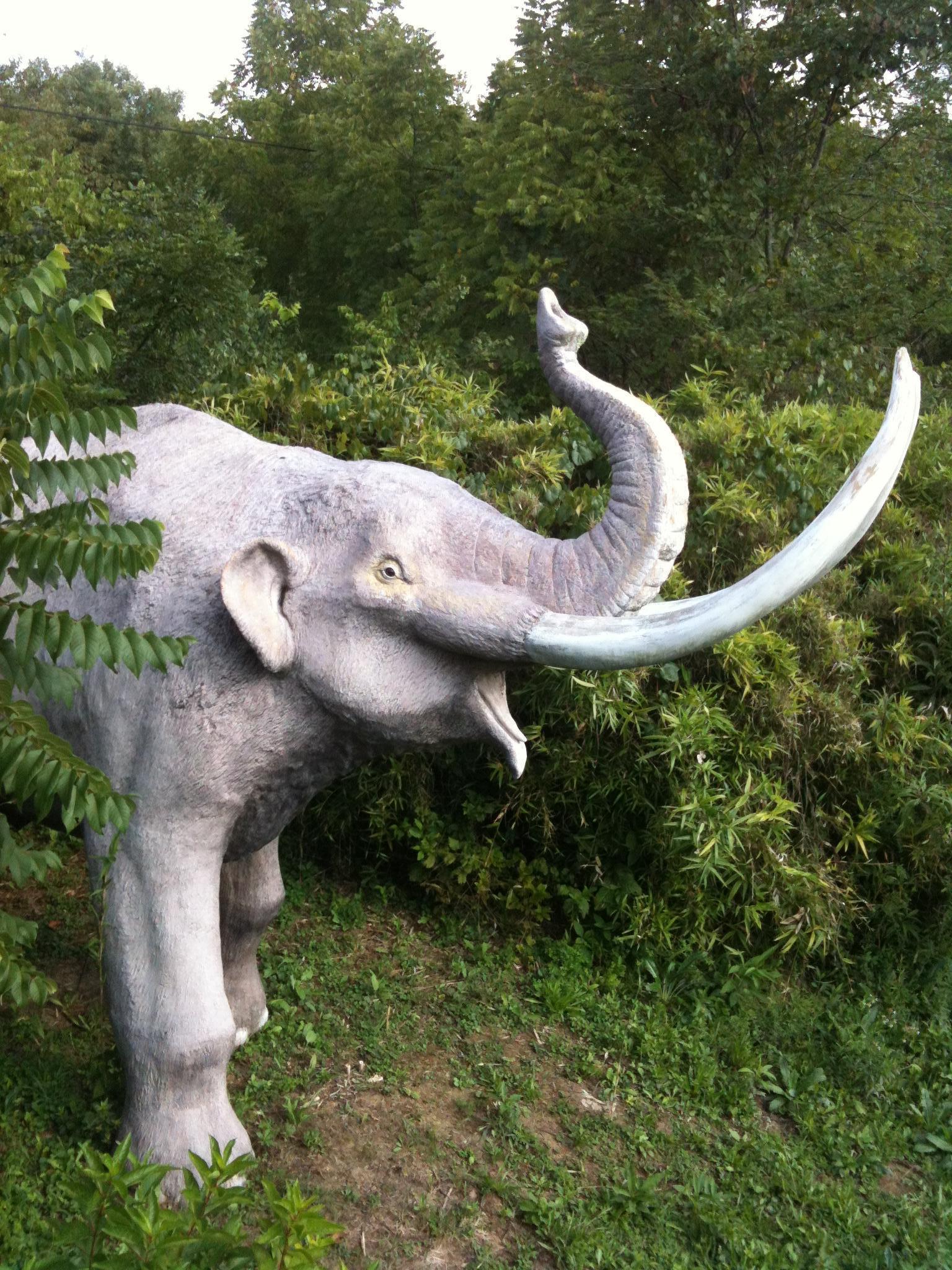 A large, light-colored mammoth statue stands among dense green foliage.
