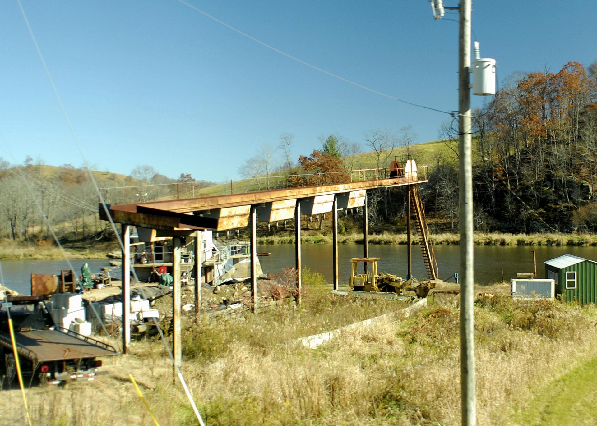 An old industrial structure with a long ramp by a river on a sunny day.