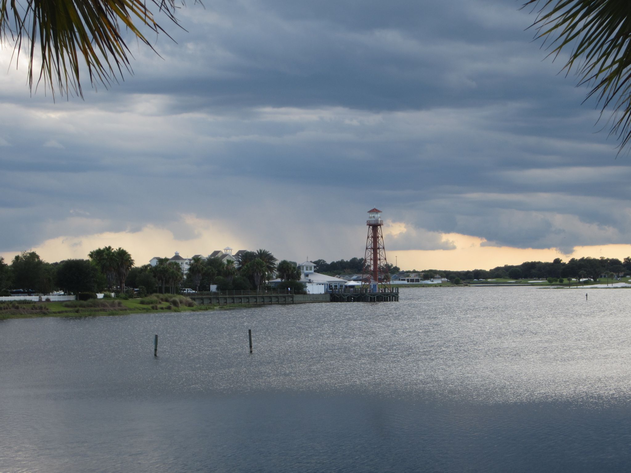 Overcast view of a red tower on a pier by water, framed by palm fronds. - The Villages loop