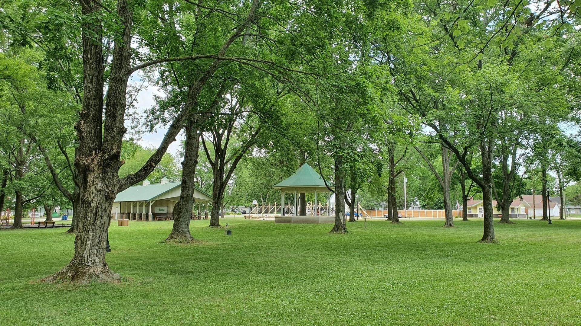 A green park with large trees, a gazebo, and distant buildings.