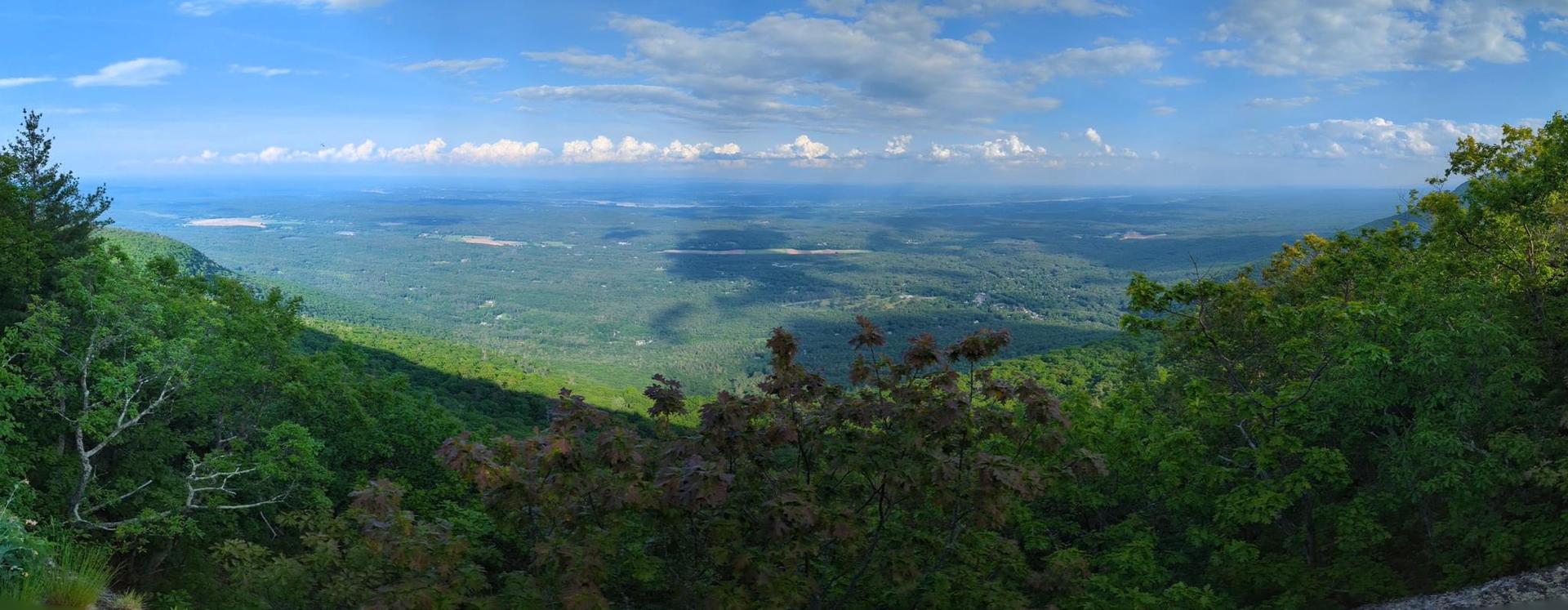Panoramic view of a vast green valley under a bright, cloudy sky.