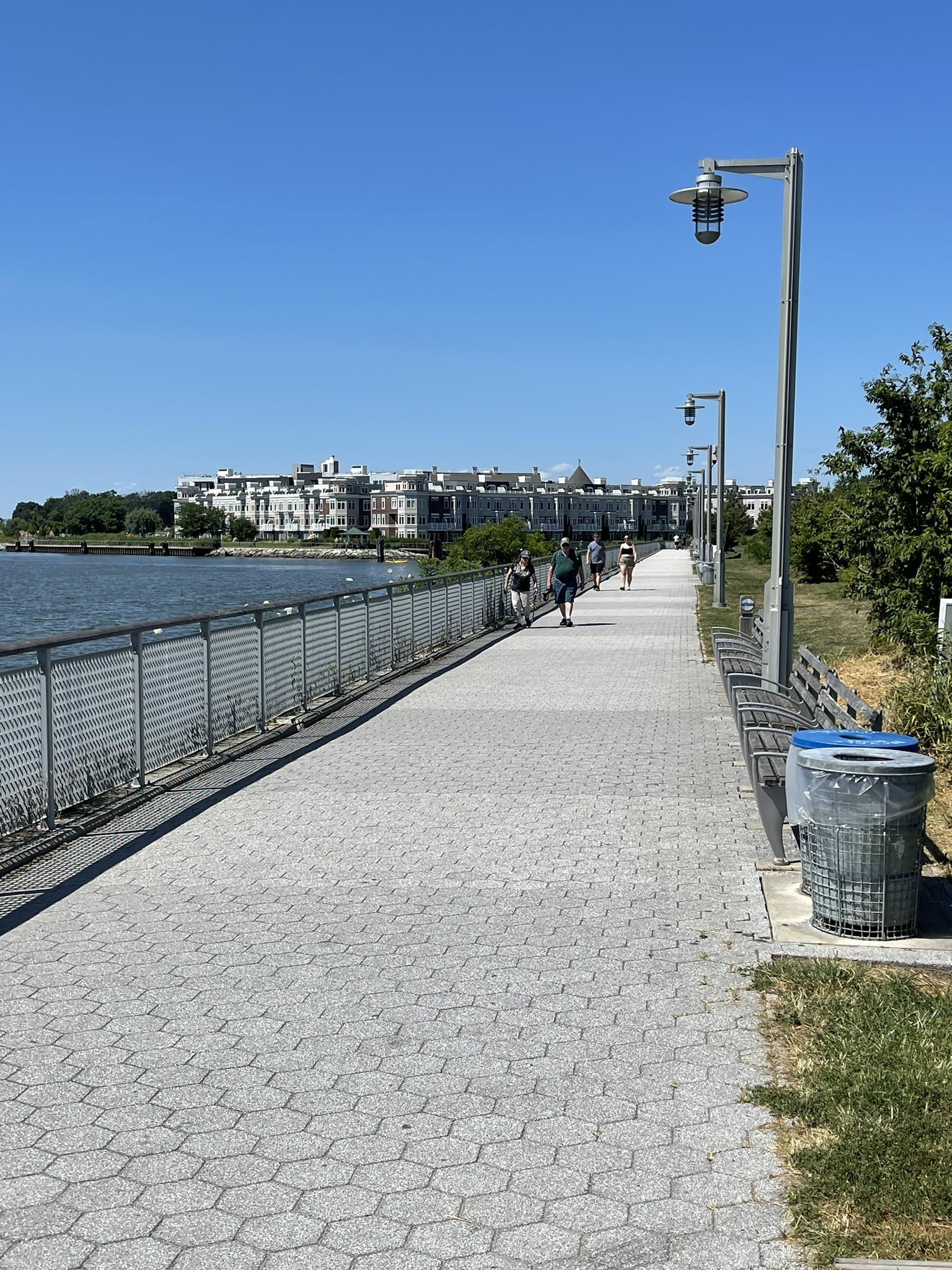 People walking on a paved waterfront path next to water and buildings. - Pierson Park and Tarrytown Riverwalk Loop