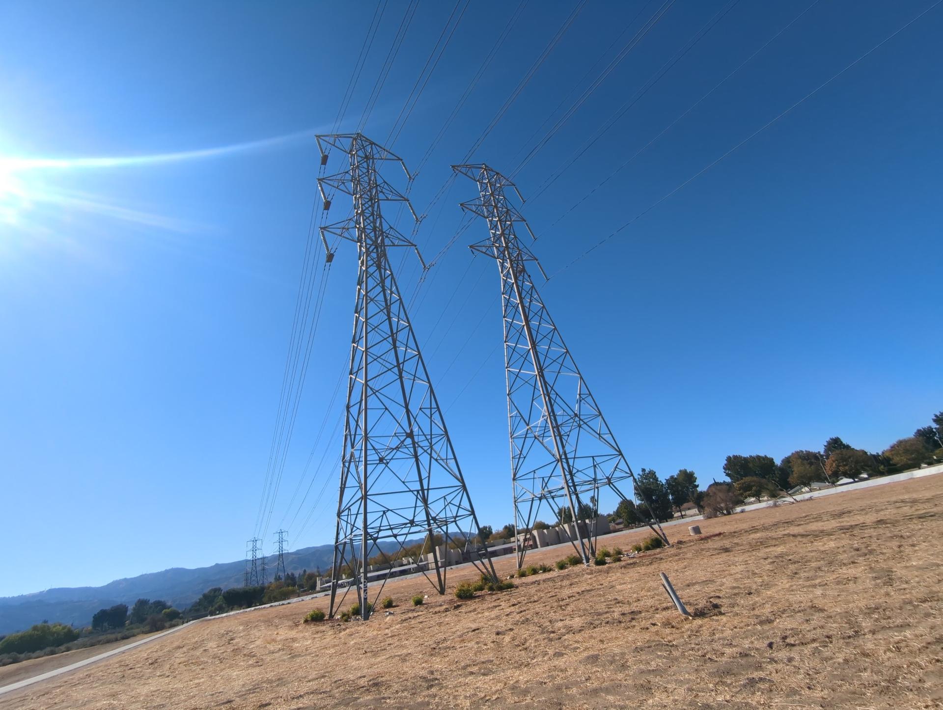 Two tall power line towers on a dry hillside under a bright blue sky.