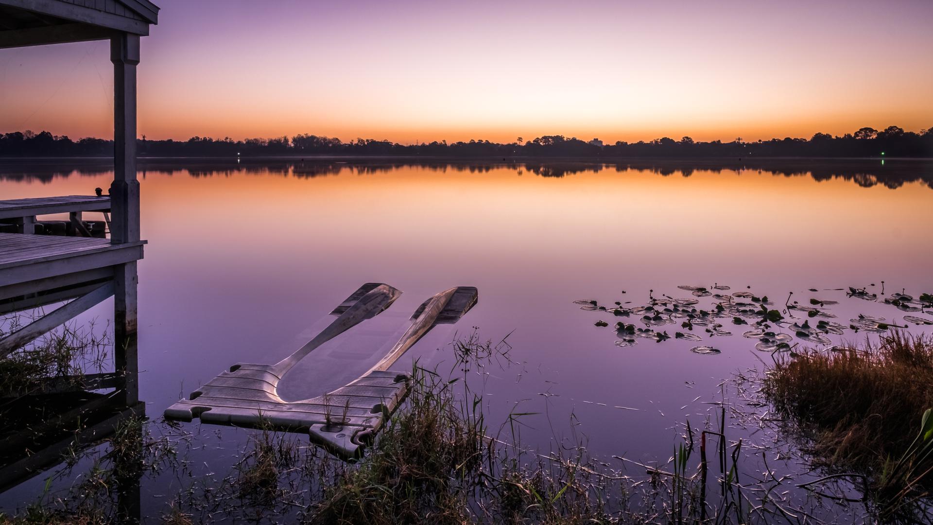 Serene lake at sunrise with a dock, floating platform, and clear kayaks.
