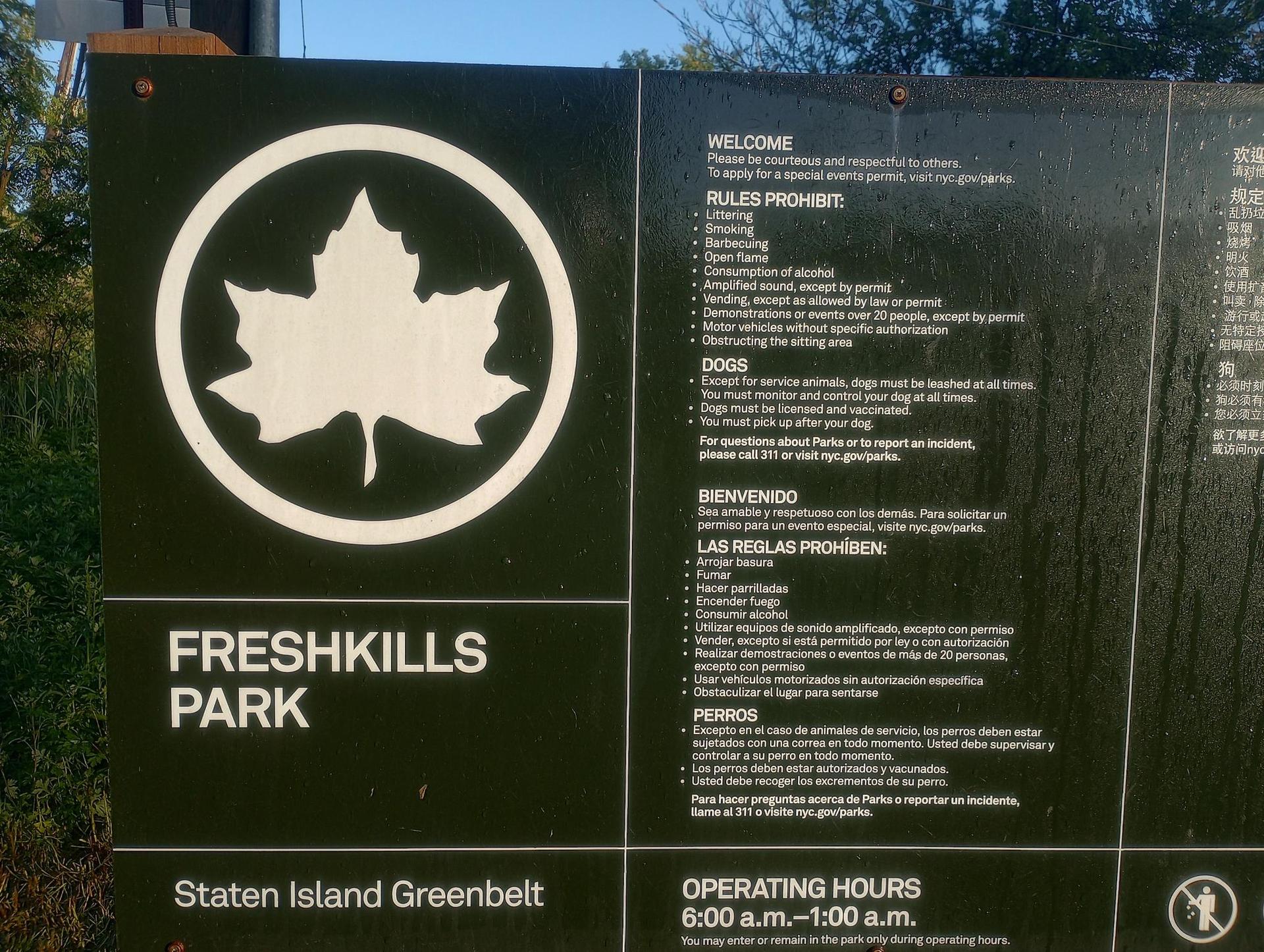Close-up of a dark park information sign with a white leaf logo.