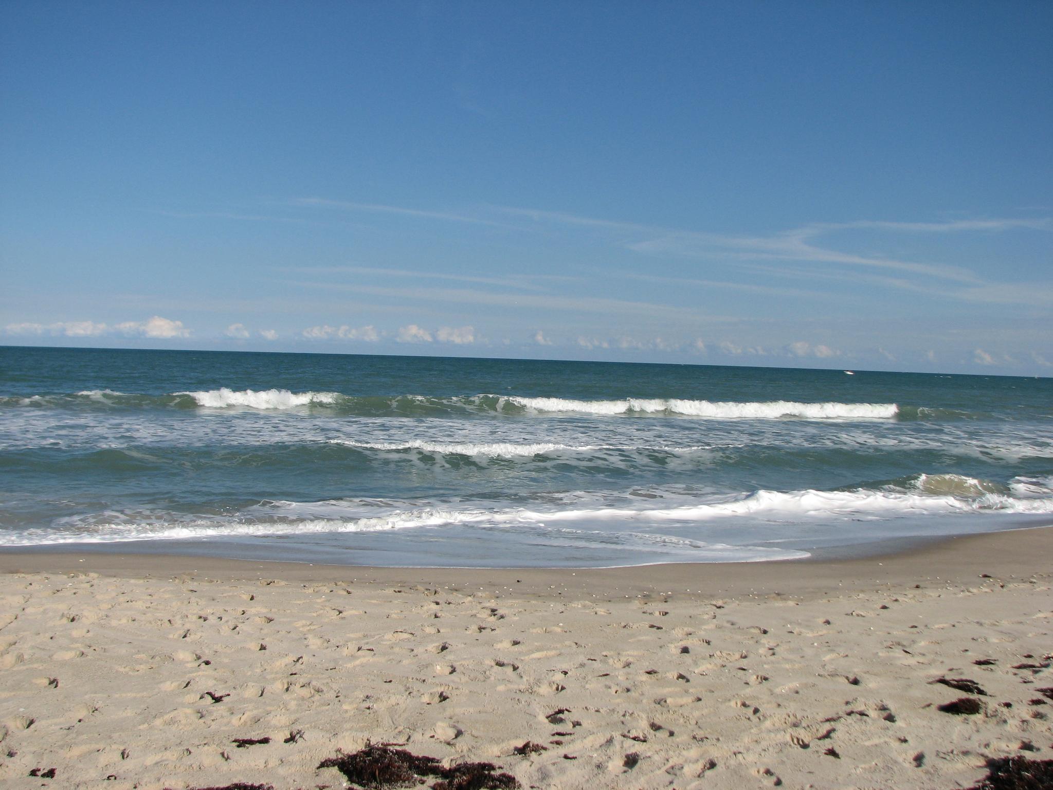 Bright sunny day at a sandy beach with ocean waves under a clear blue sky.