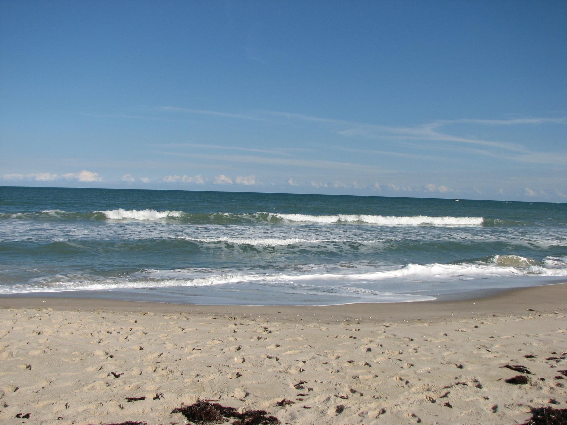 Bright sunny day at a sandy beach with ocean waves under a clear blue sky.