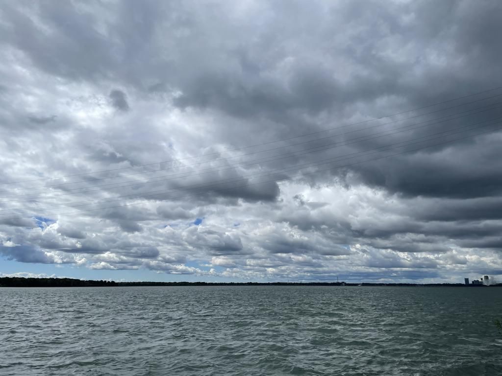 Choppy water under a vast, dark, overcast sky with distant land. - Shoreline Trail