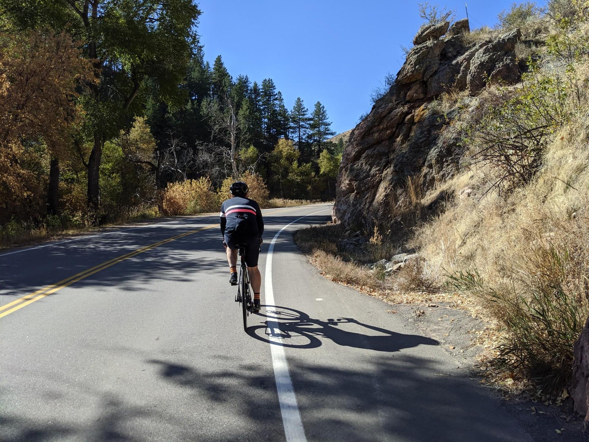 Cyclist on an asphalt road next to a rocky hillside, sunny day.