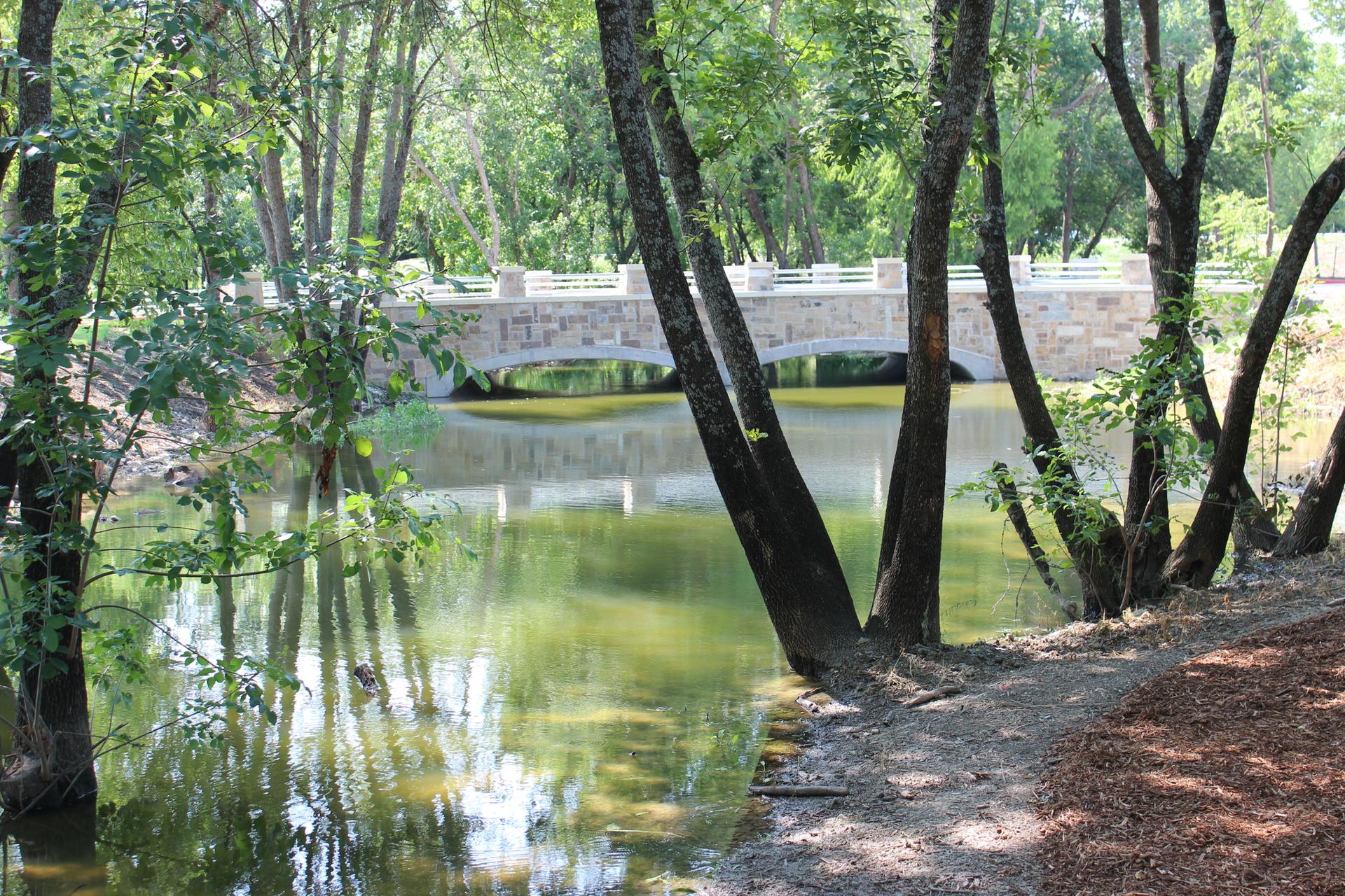 Stone bridge arches over calm green water, framed by trees.