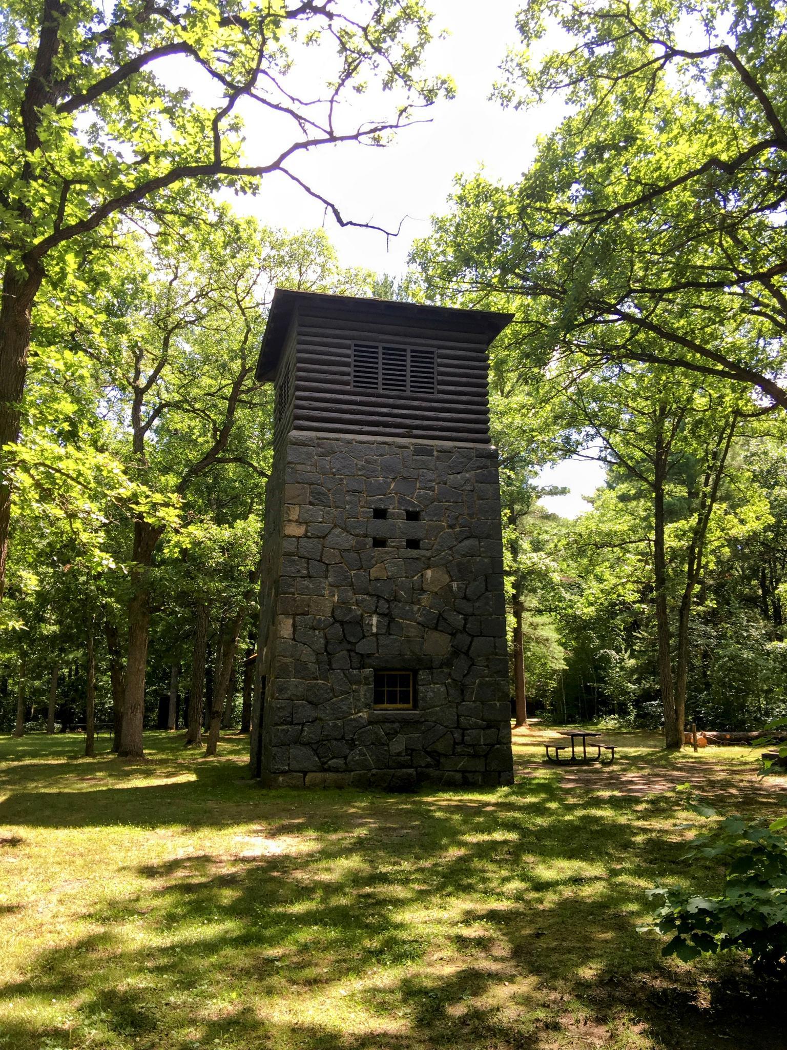 A stone and wood tower stands among tall trees on a sunny day.