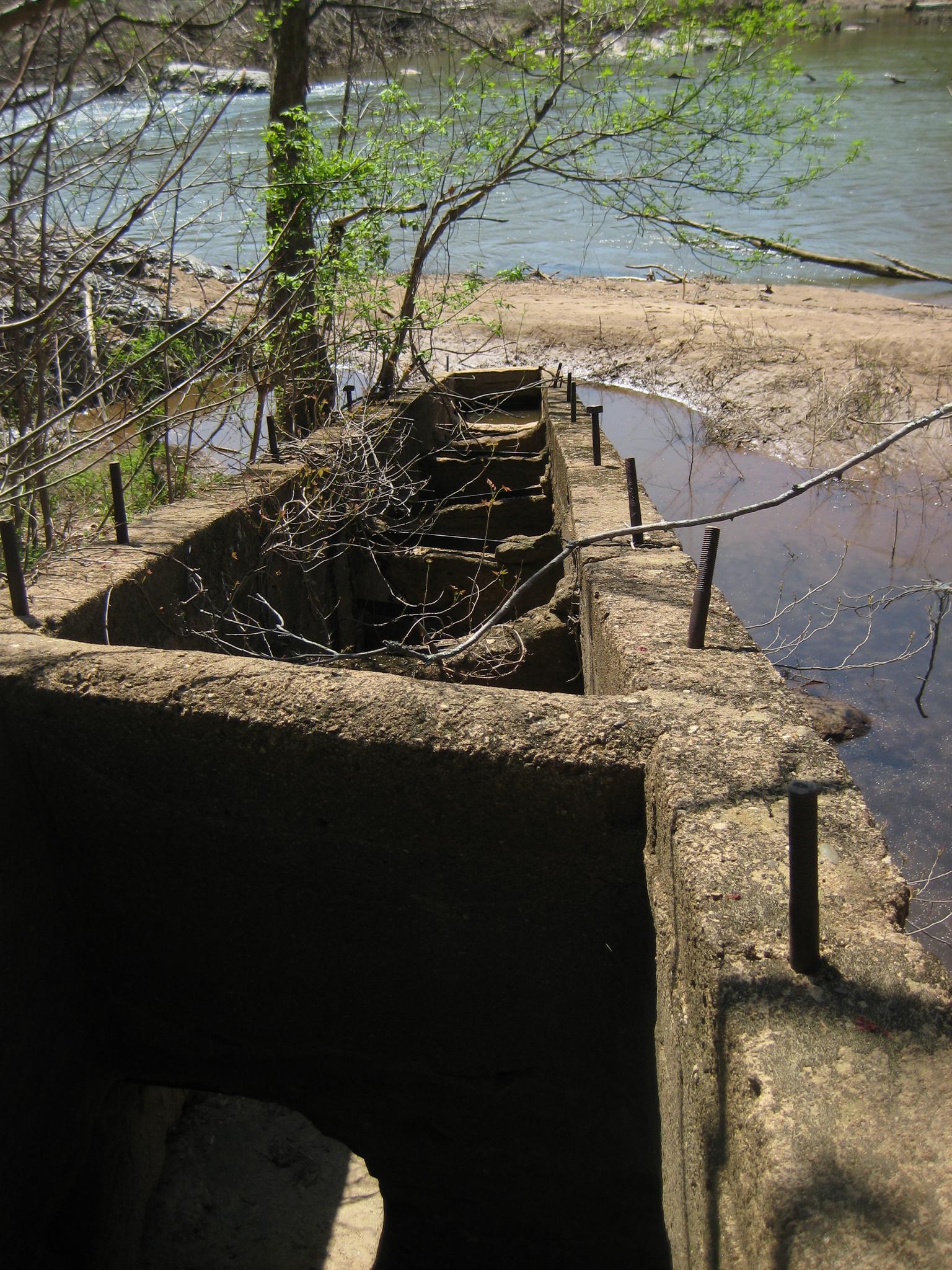 Concrete structure with rebar next to a river under bright daylight.
