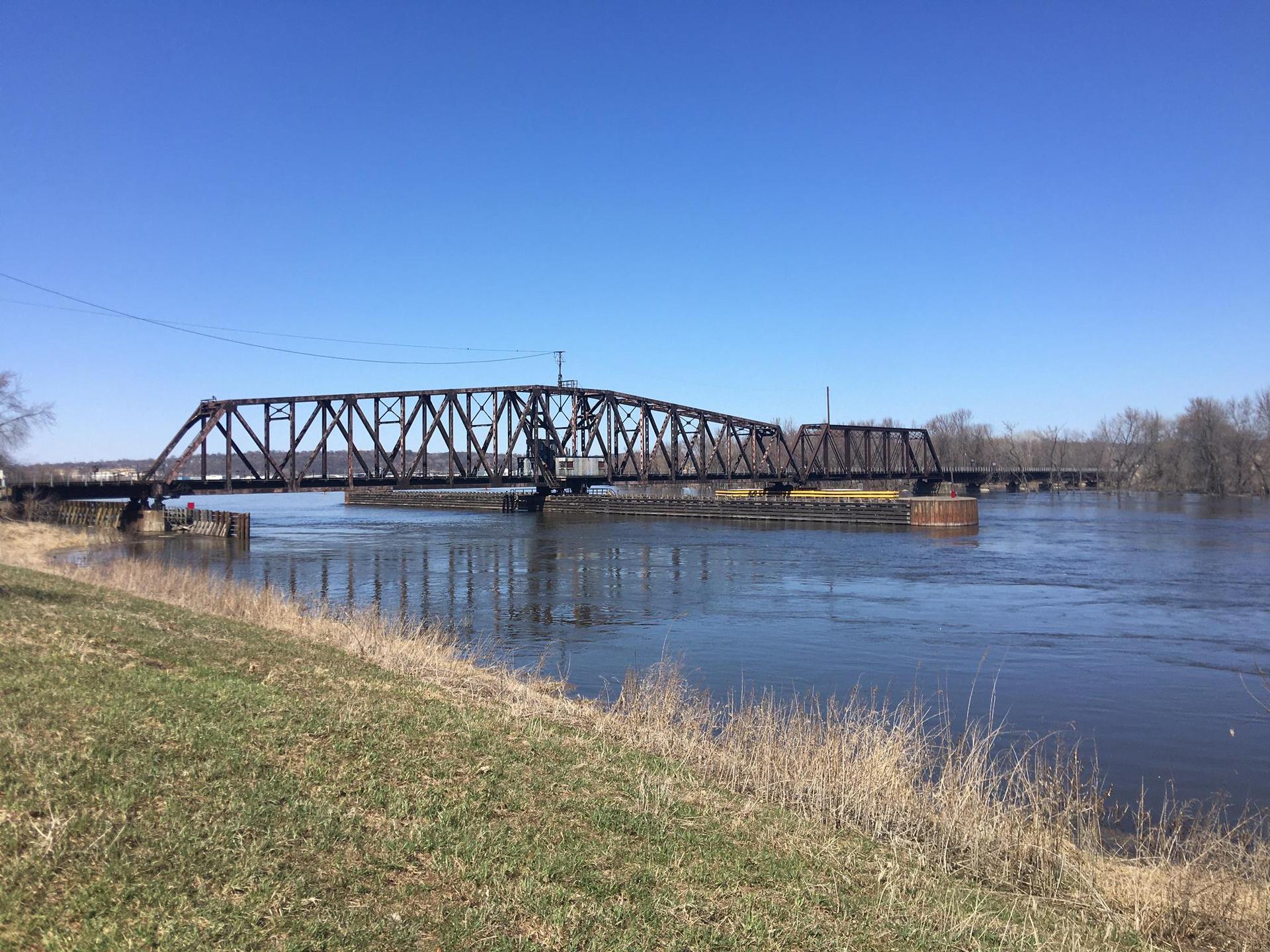 Large metal truss bridge spans a wide river under a clear blue sky.