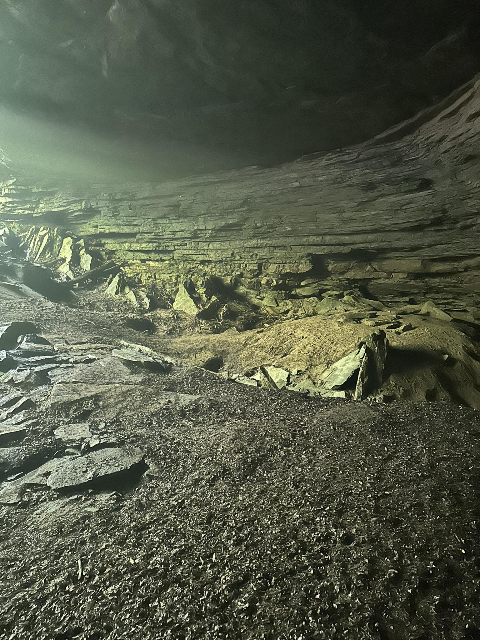 Dimly lit cave interior with layered rock walls and debris on the floor.