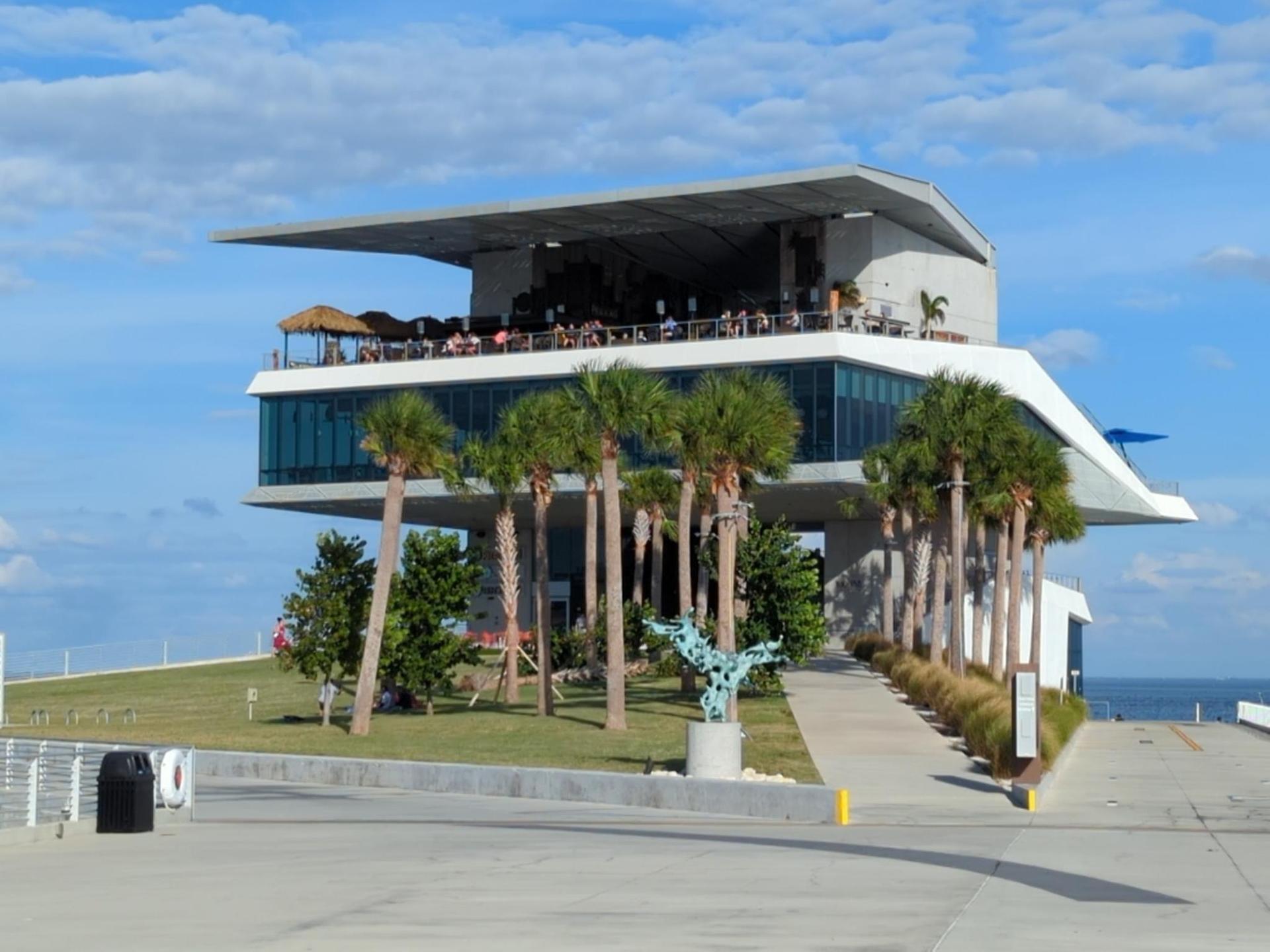 Modern multi-story building with people on deck, surrounded by palm trees.