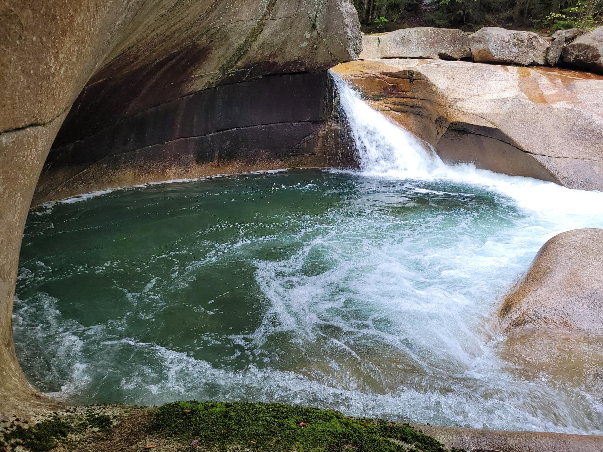 Small waterfall flows into a deep green pool surrounded by smooth, wet rocks.