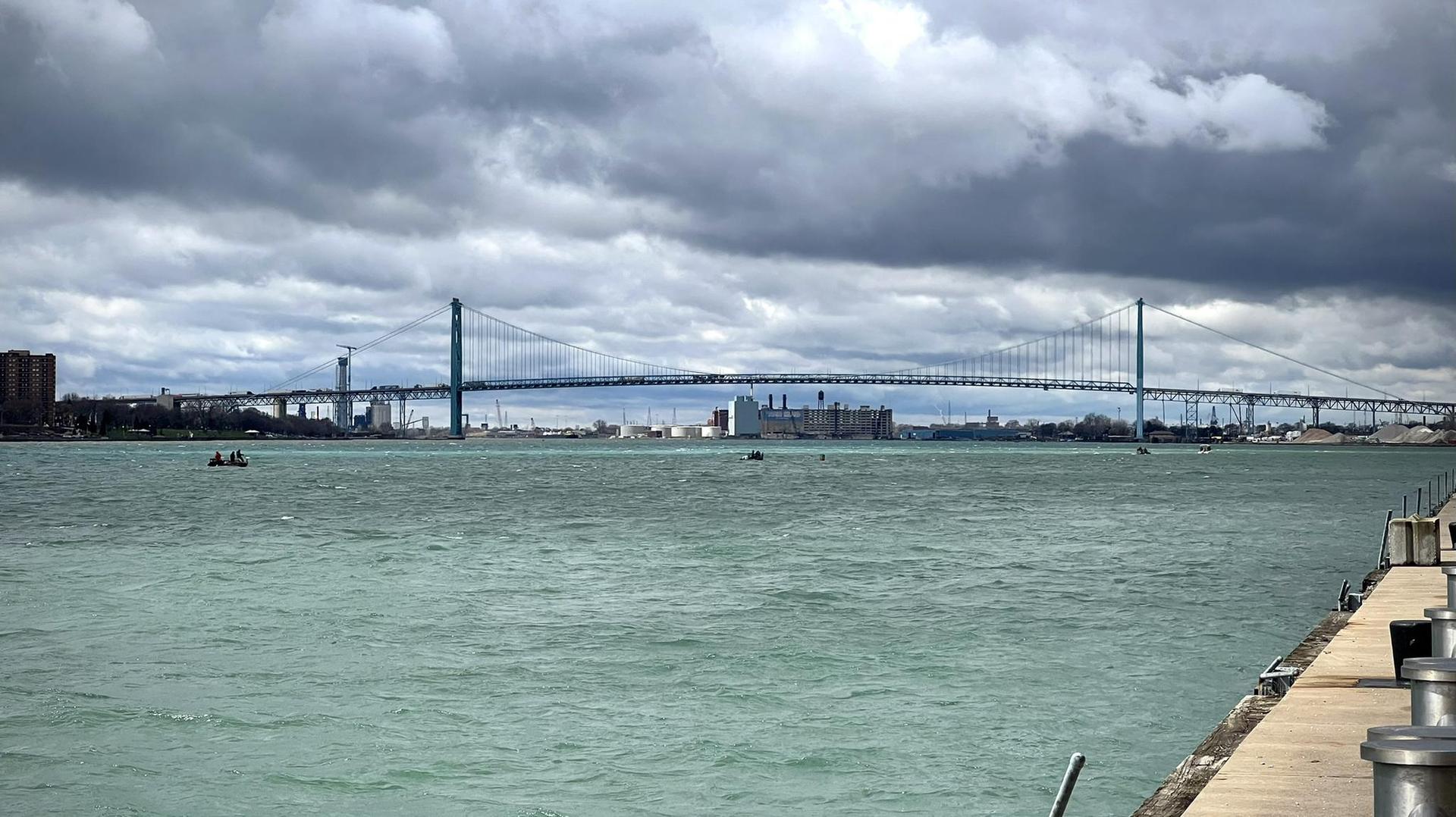 A large suspension bridge spans wide water under a cloudy sky.