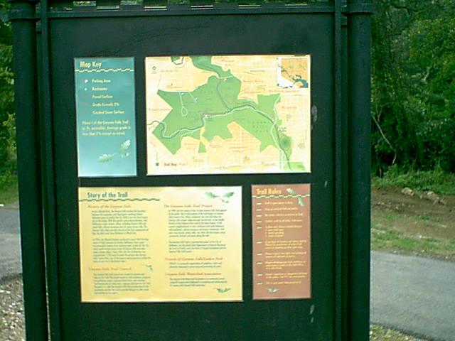 An outdoor information board with maps and text stands by a path.