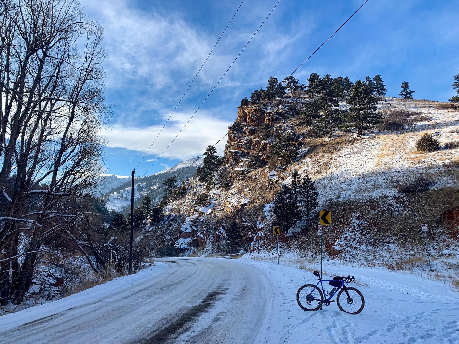 Bicycle parked on a snowy mountain road under a bright, cloudy sky.