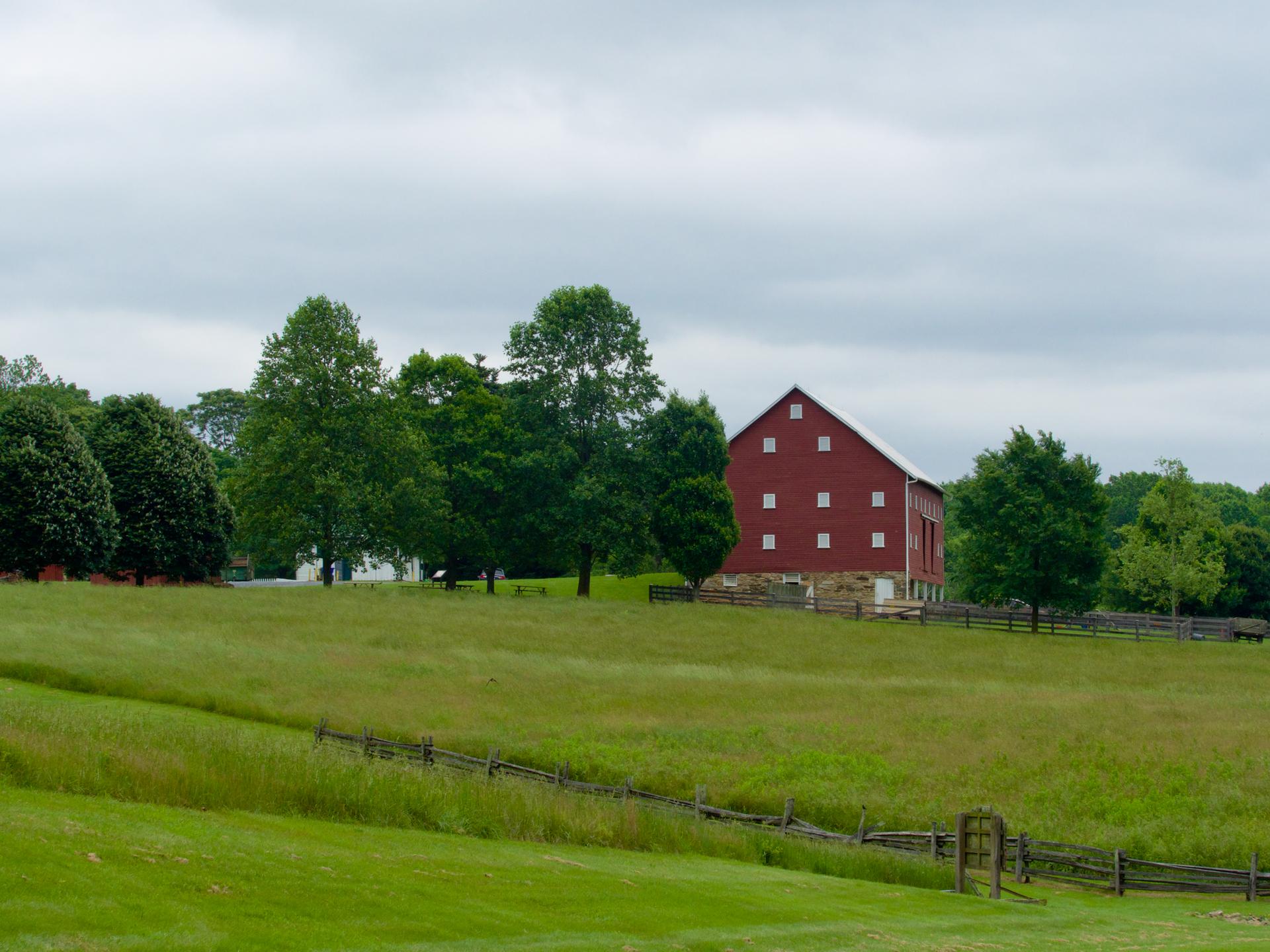 A red barn stands on a green hill under an overcast sky.