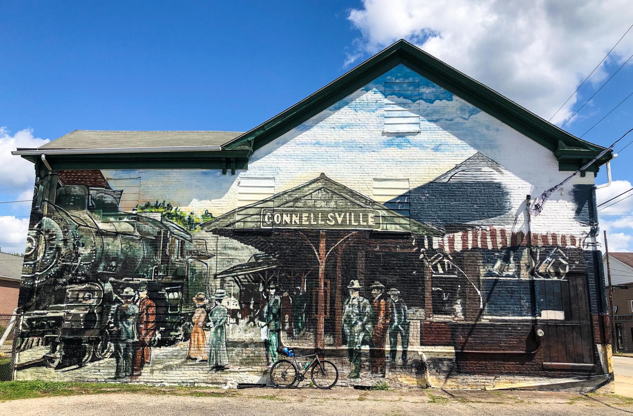 A vibrant mural of a train station scene on a building wall. - Connellsville – Youghiogheny River loop from Connellsville