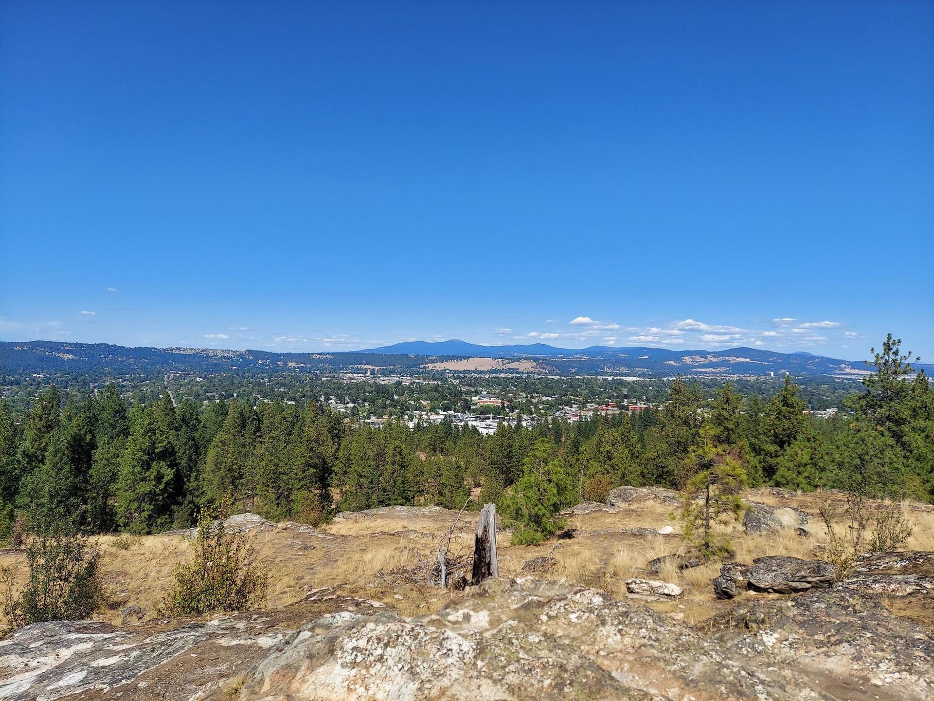 Panoramic view from a rocky hill overlooking a town and distant mountains.