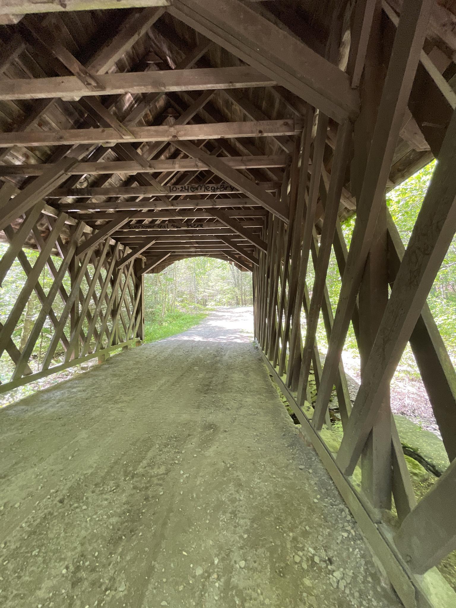 Inside a wooden covered bridge with a dirt path leading to light.