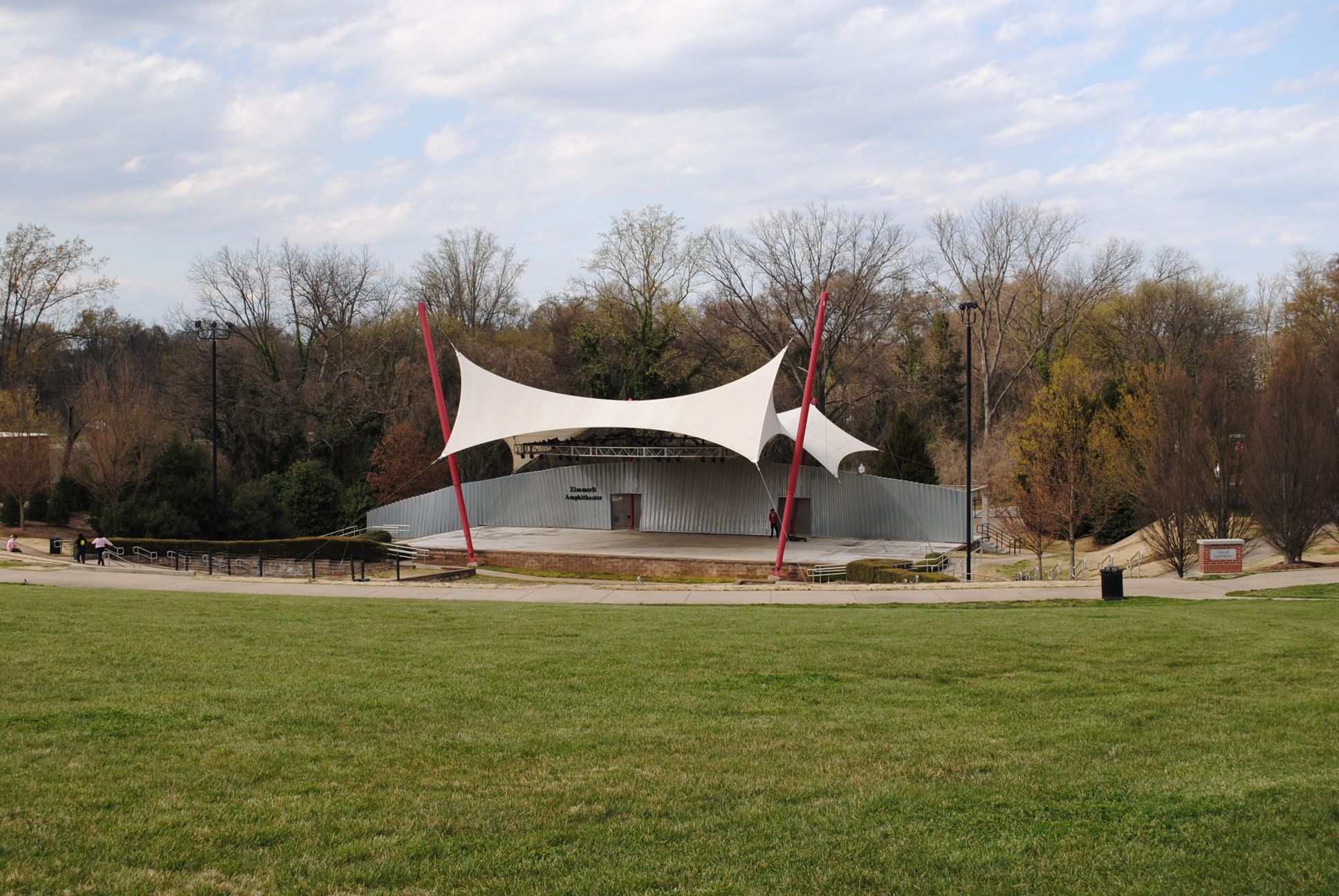 Outdoor amphitheater with white tensile roof, green field, and bare trees under overcast sky. - Mary Black Rail Trail