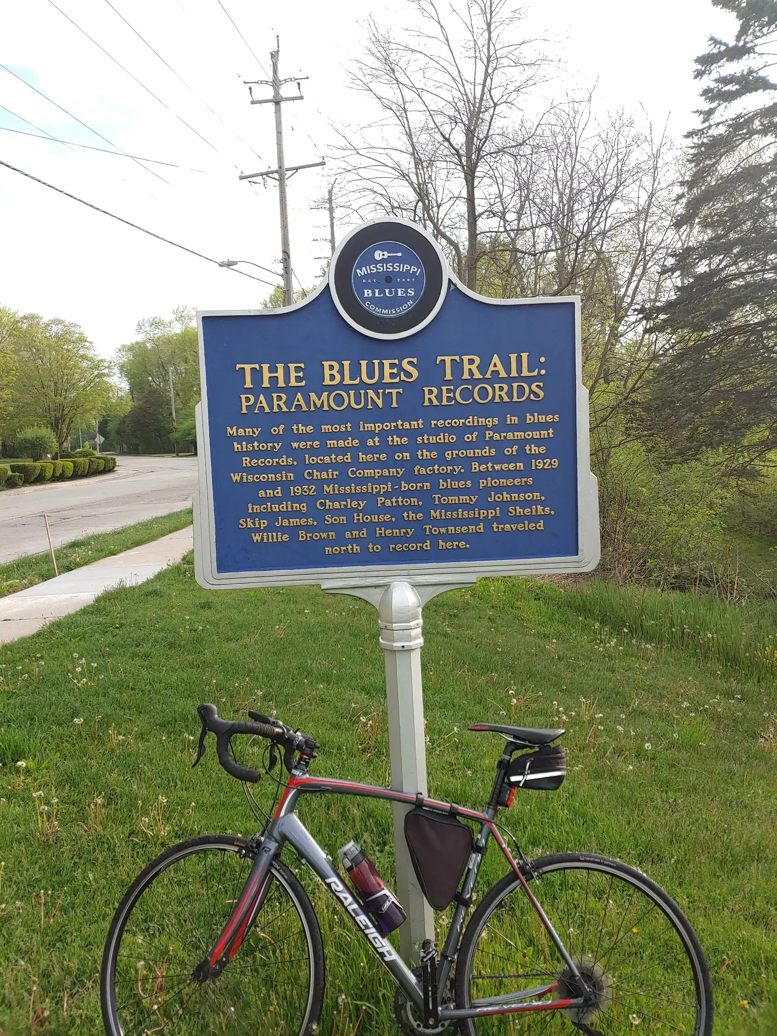 A bicycle is parked in front of a blue historical marker on a grassy lawn.