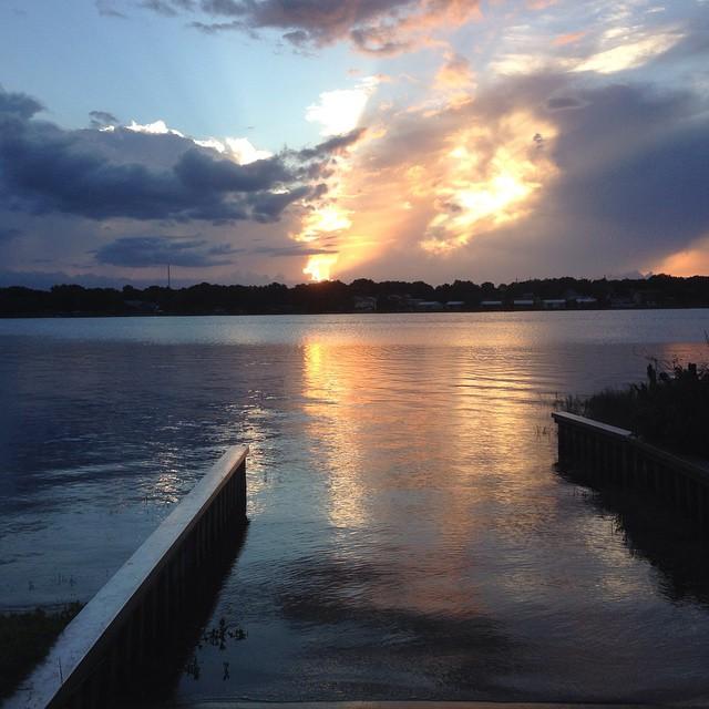 Dramatic sunset over water with colorful clouds and reflections, viewed from a dock.