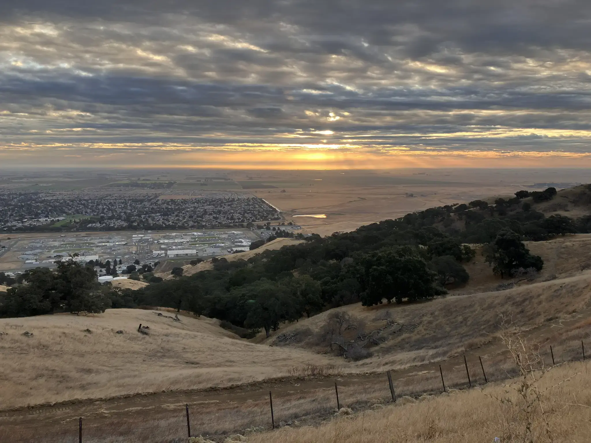 Golden sunset over a valley town, seen from dry, grassy hills.