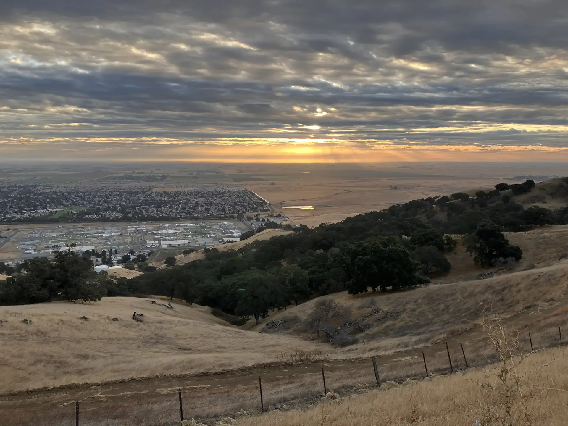 Golden sunset over a valley town, seen from dry, grassy hills.