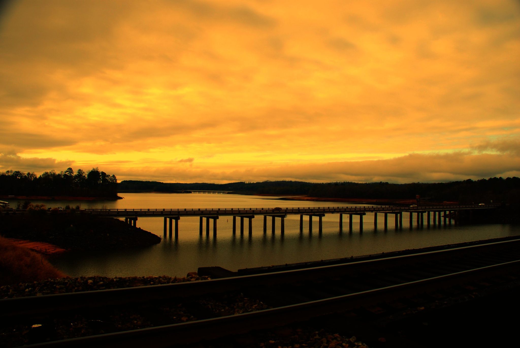 A long bridge spans dark water under a dramatic golden and orange sky. - Lake Hartwell loop