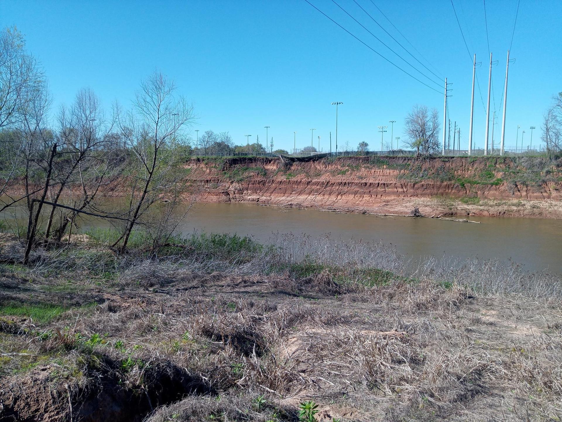A wide river flows past a steep, eroded bank under a clear sky.