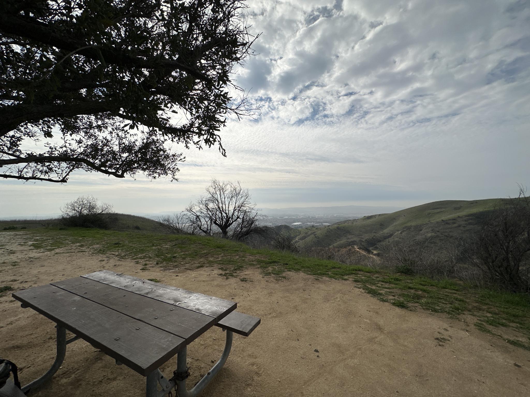 Picnic table on a hilltop overlooking a vast valley under a cloudy sky.