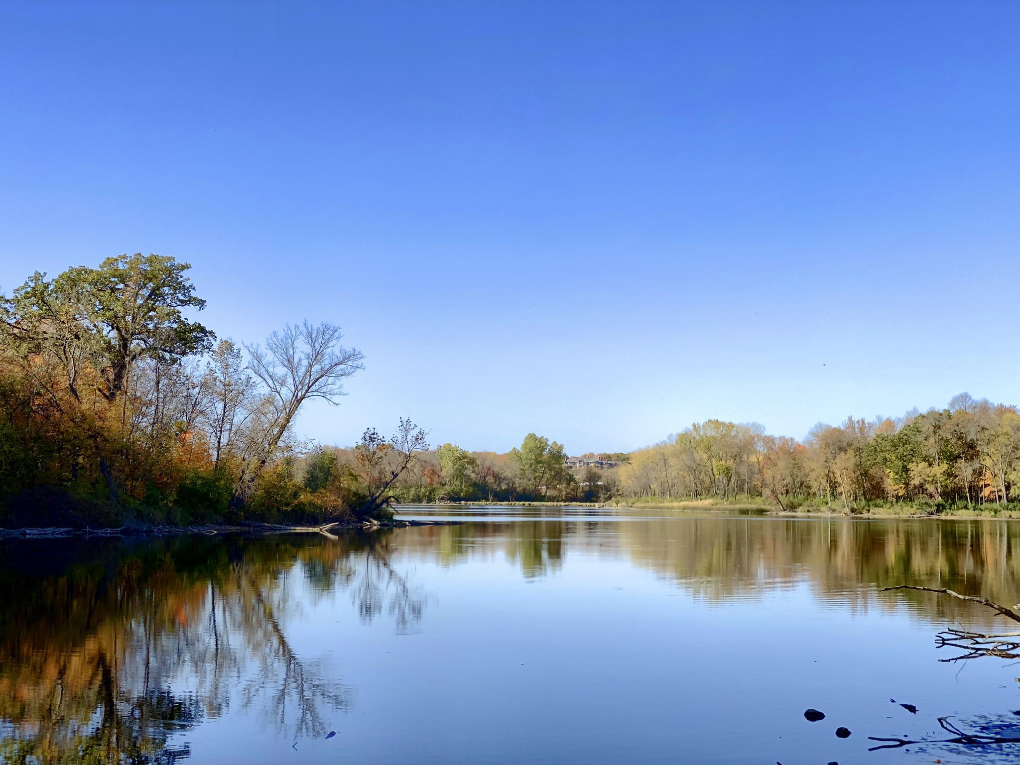 Calm lake reflecting a clear blue sky and autumn trees on its banks.