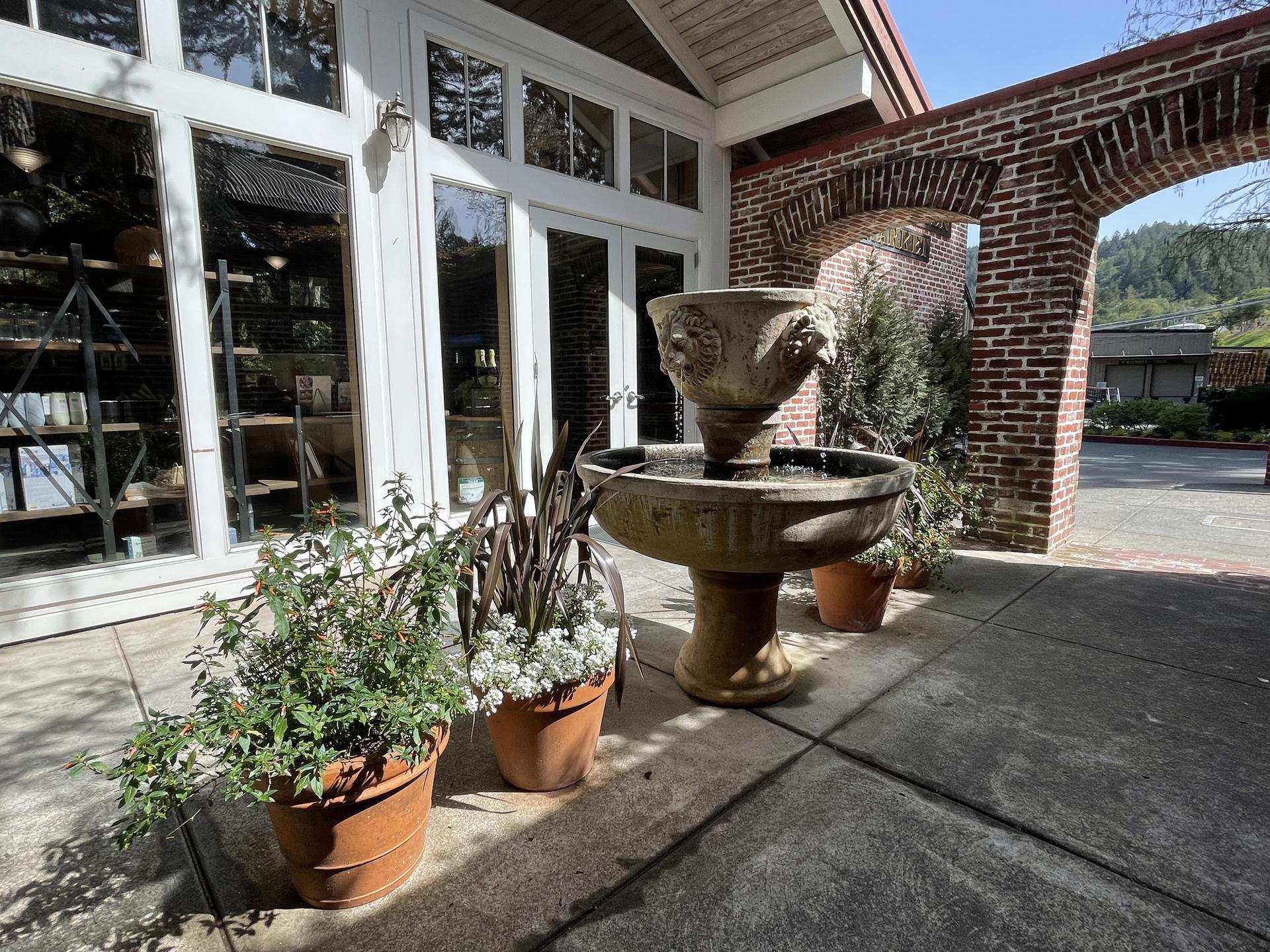 An outdoor tiered fountain with potted plants next to a building entrance.