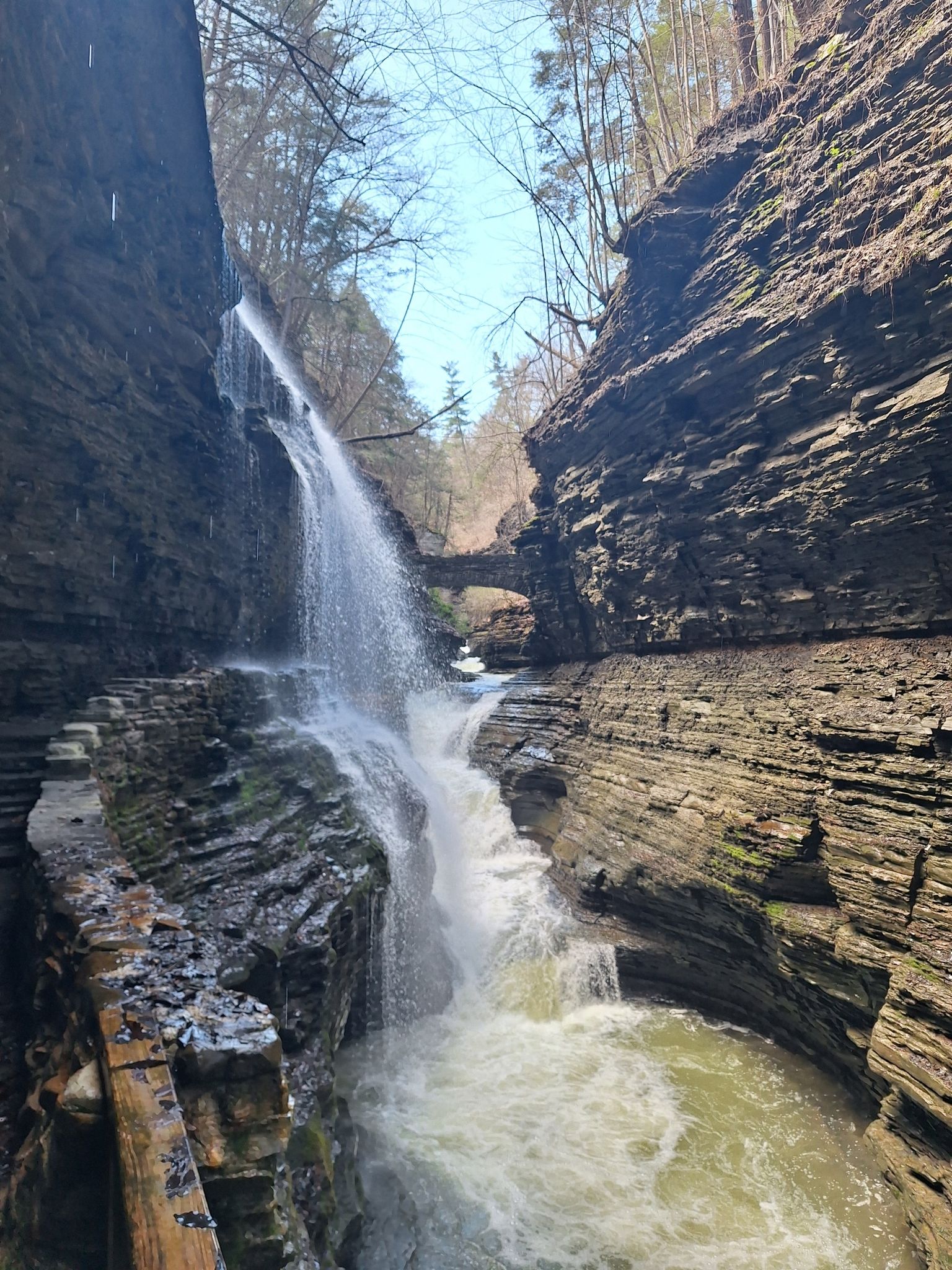 Waterfall cascading down a rocky gorge with a wooden walkway, bright daylight. - Gorge and Indian Trail