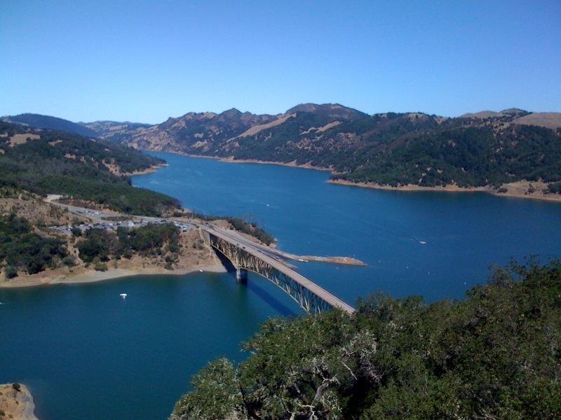 Long bridge spans a wide blue lake surrounded by forested mountains.